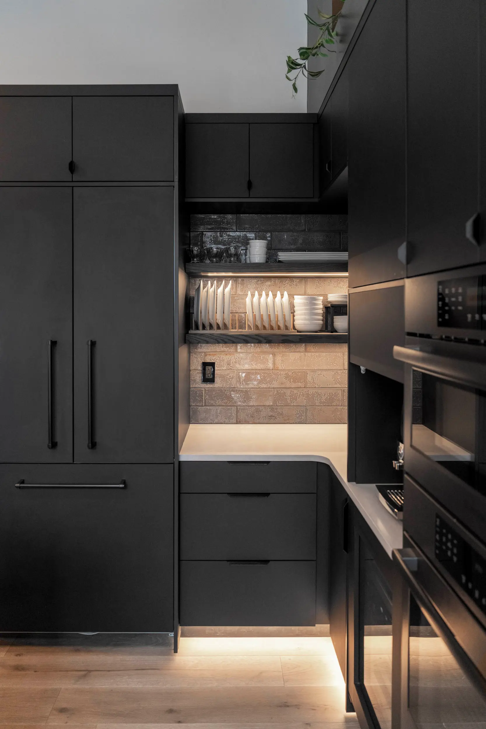 Modern kitchen corner with matte black cabinets, white countertop, wooden floor, and under-cabinet lighting.