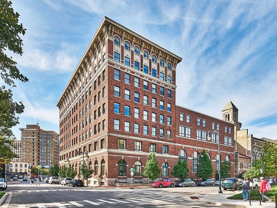 Historic multi-story brick building with arched windows on a city street corner under a blue sky.