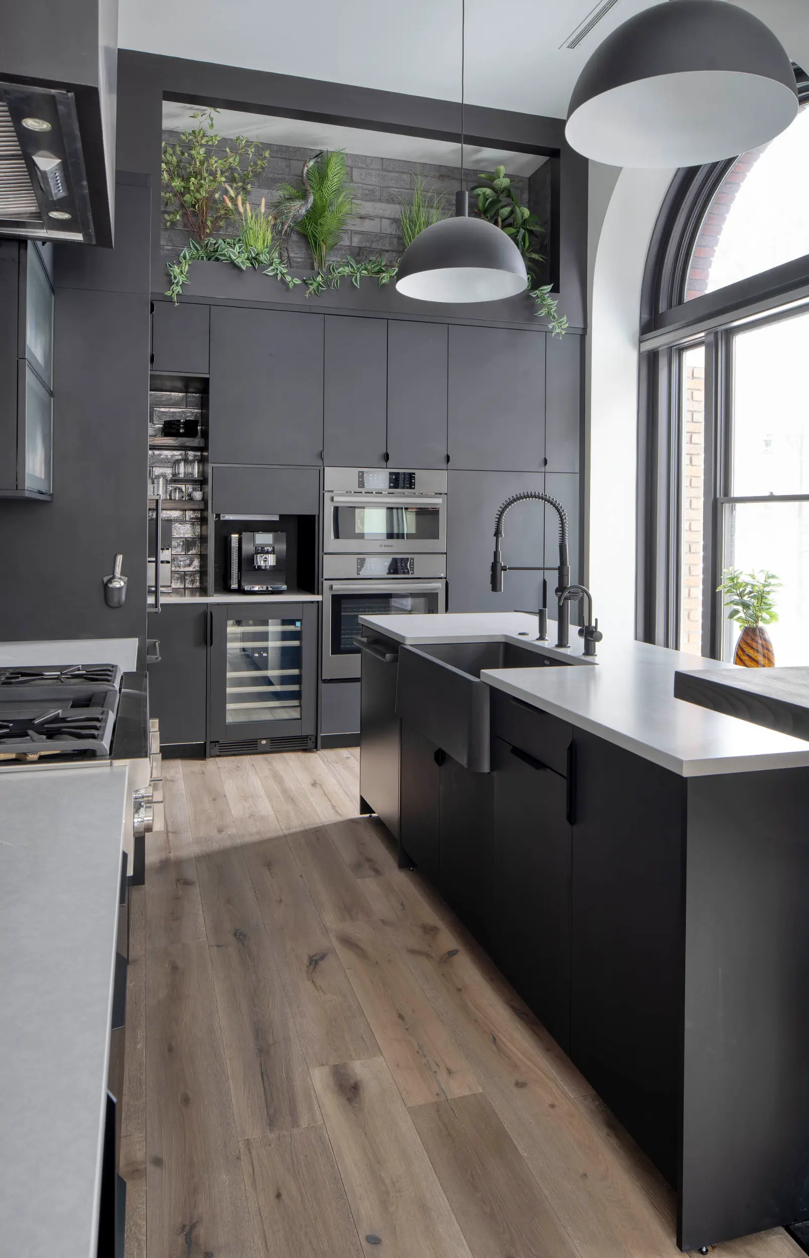 Modern kitchen with black cabinets, built-in ovens, a black sink, pendant lights, and a large window.