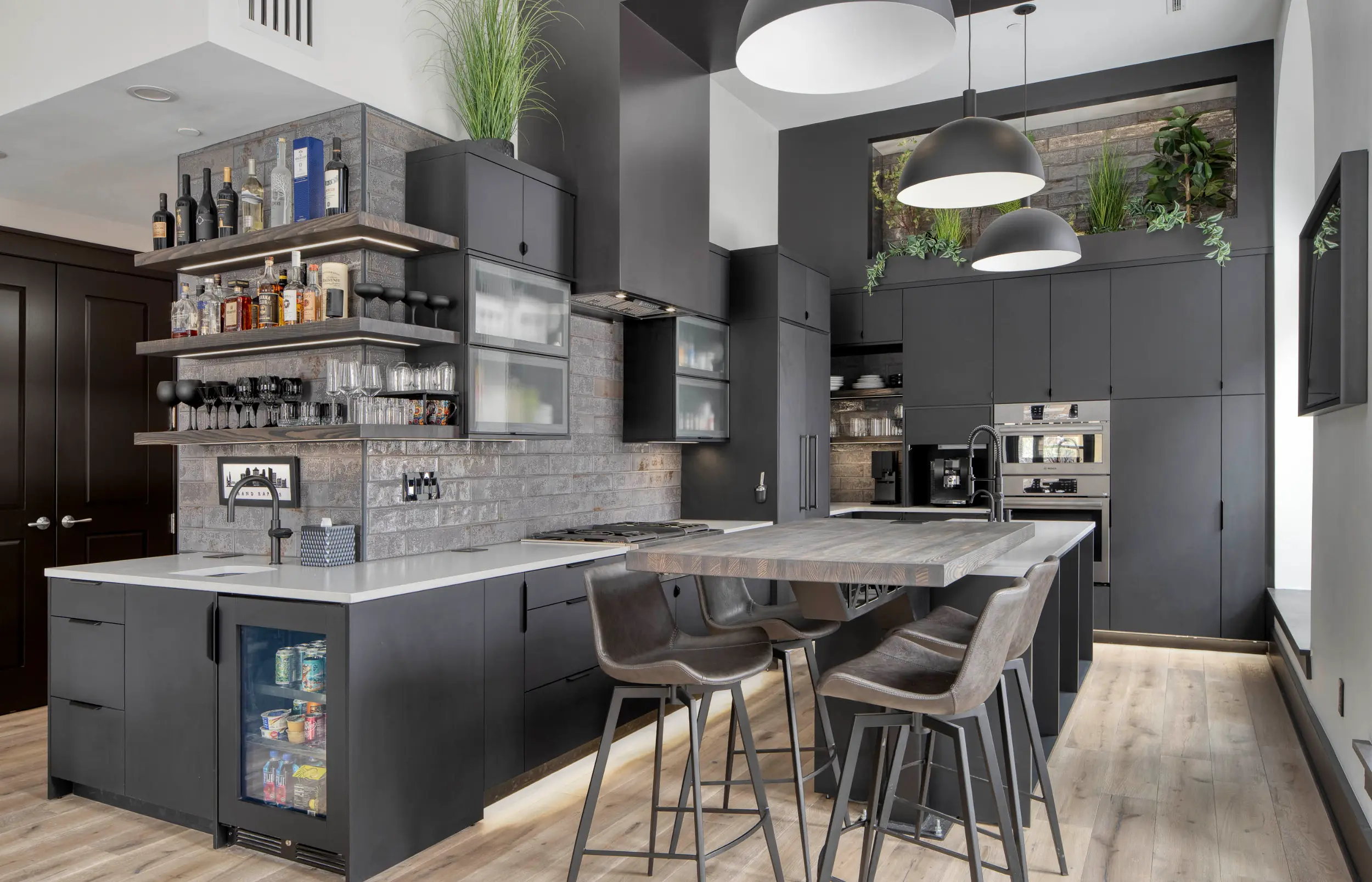 Modern kitchen with black cabinets, island with stools, shelves with glassware and bottles, and hanging lights.