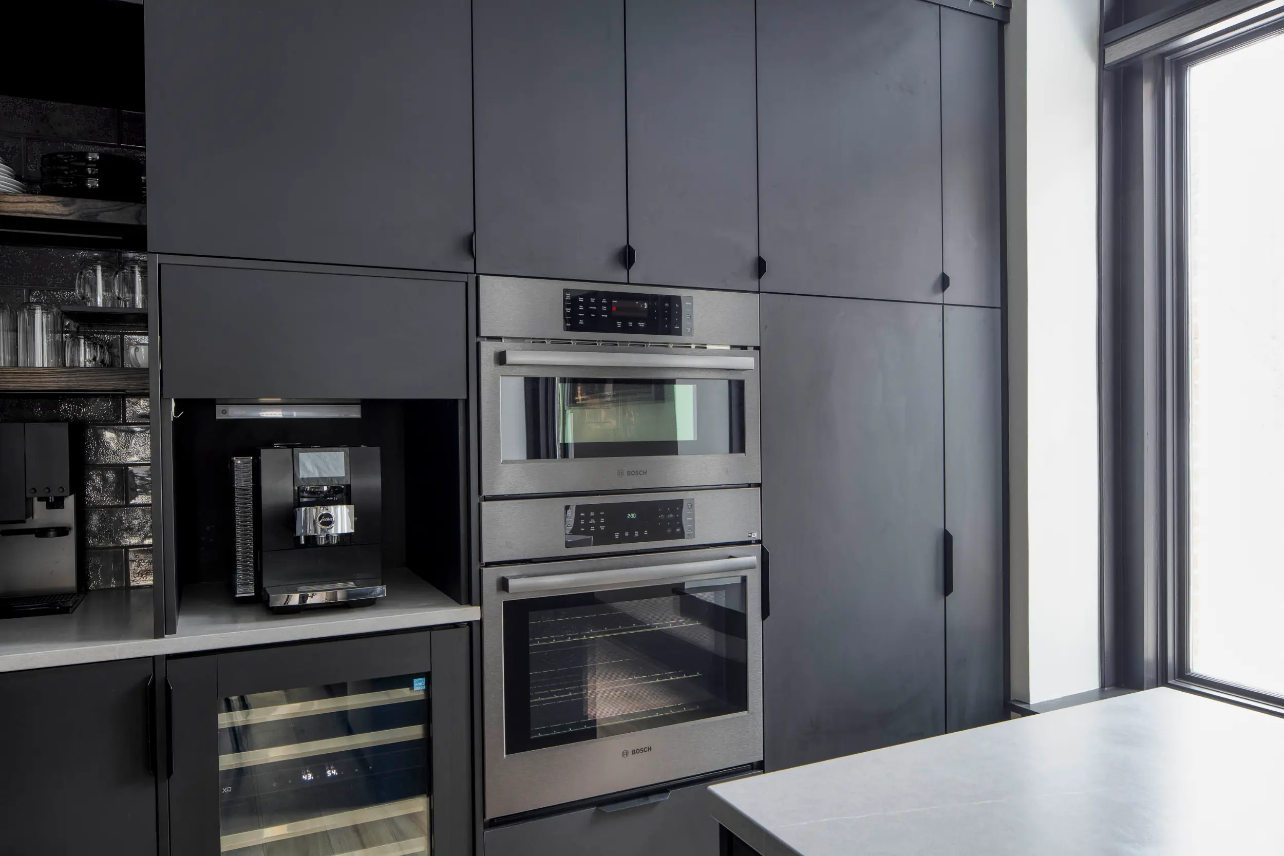 Modern kitchen with black cabinets, built-in coffee machine, wine cooler, and double stainless steel ovens.