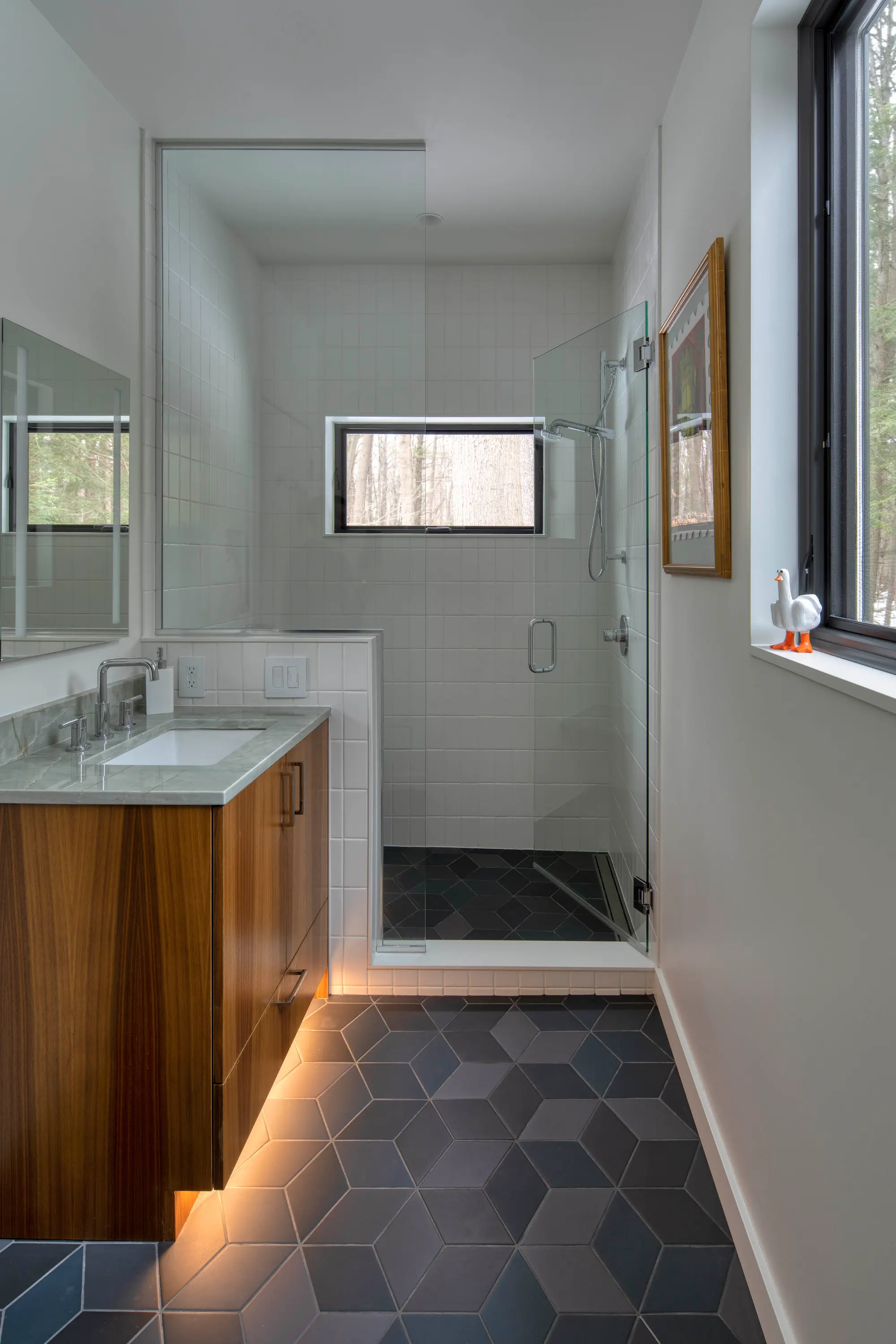 Modern bathroom with hexagonal tiles, wooden floating vanity, glass shower, and small window with duck figure.
