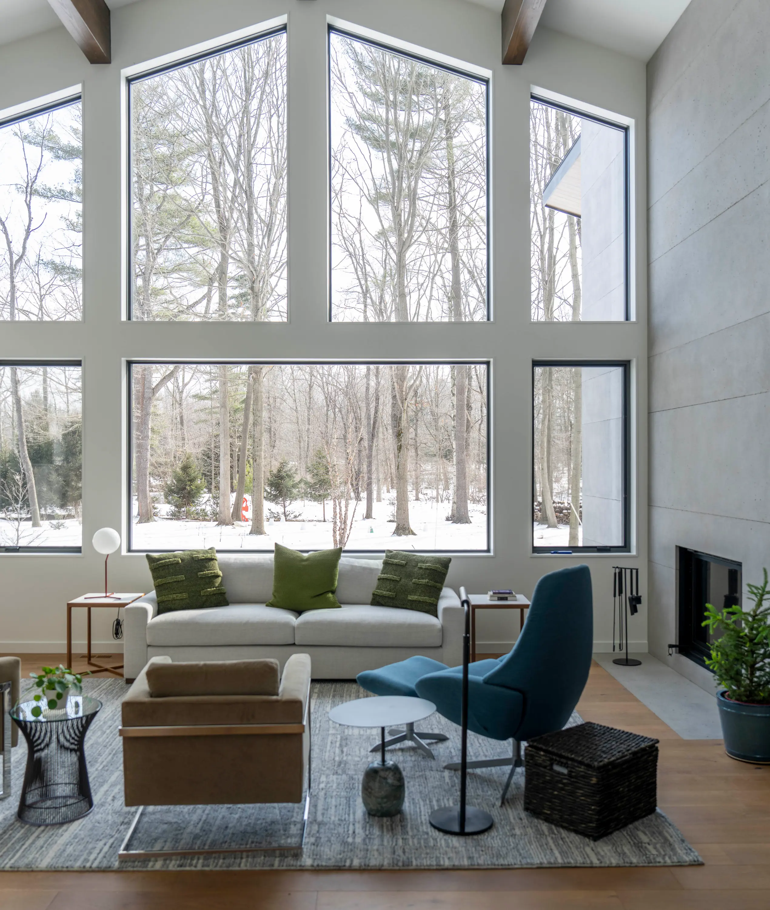 Modern living room with large windows showing a snowy wooded landscape outside.
