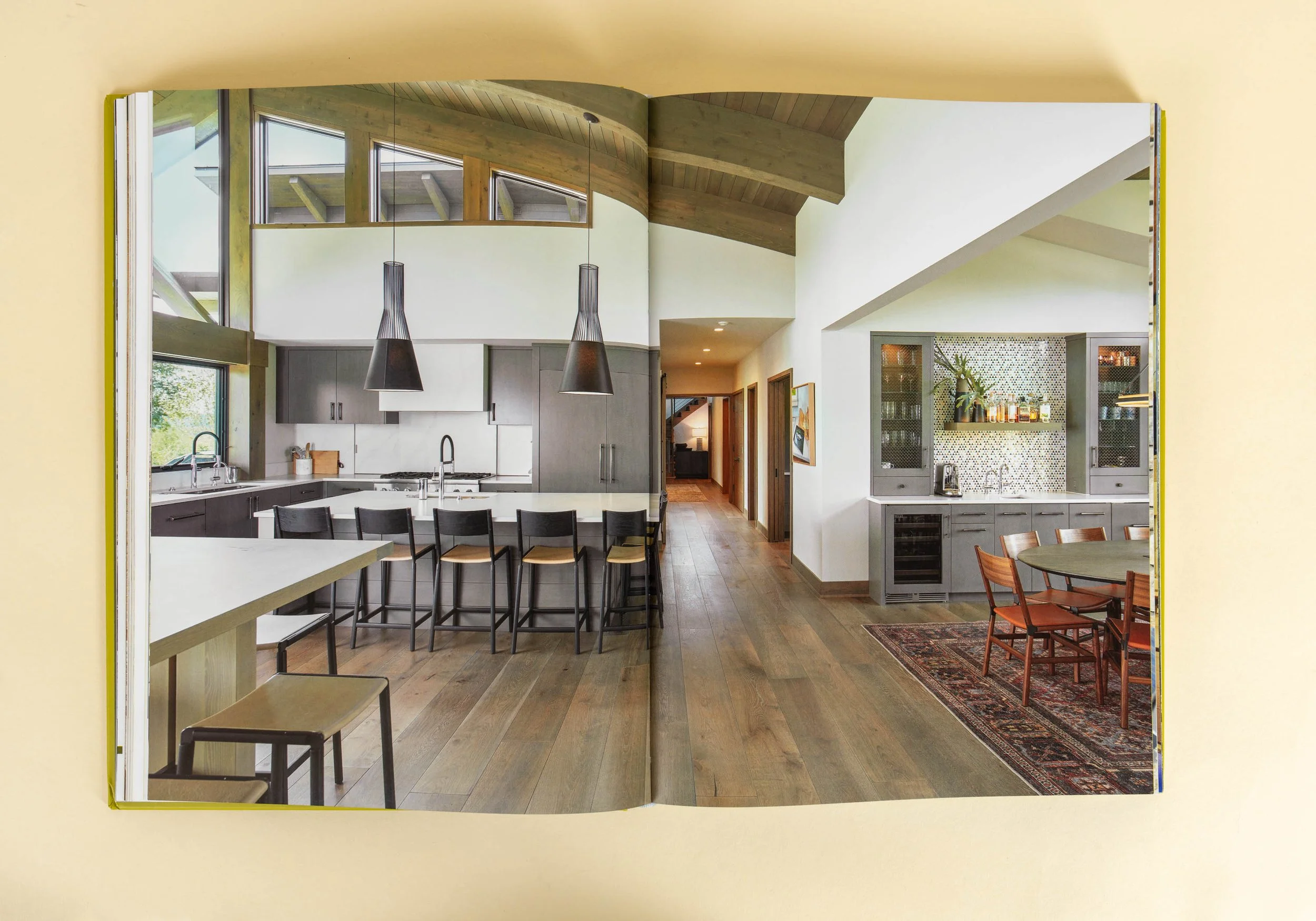 Modern open kitchen and dining area with large island, bar stools, pendant lights, and wooden floors.