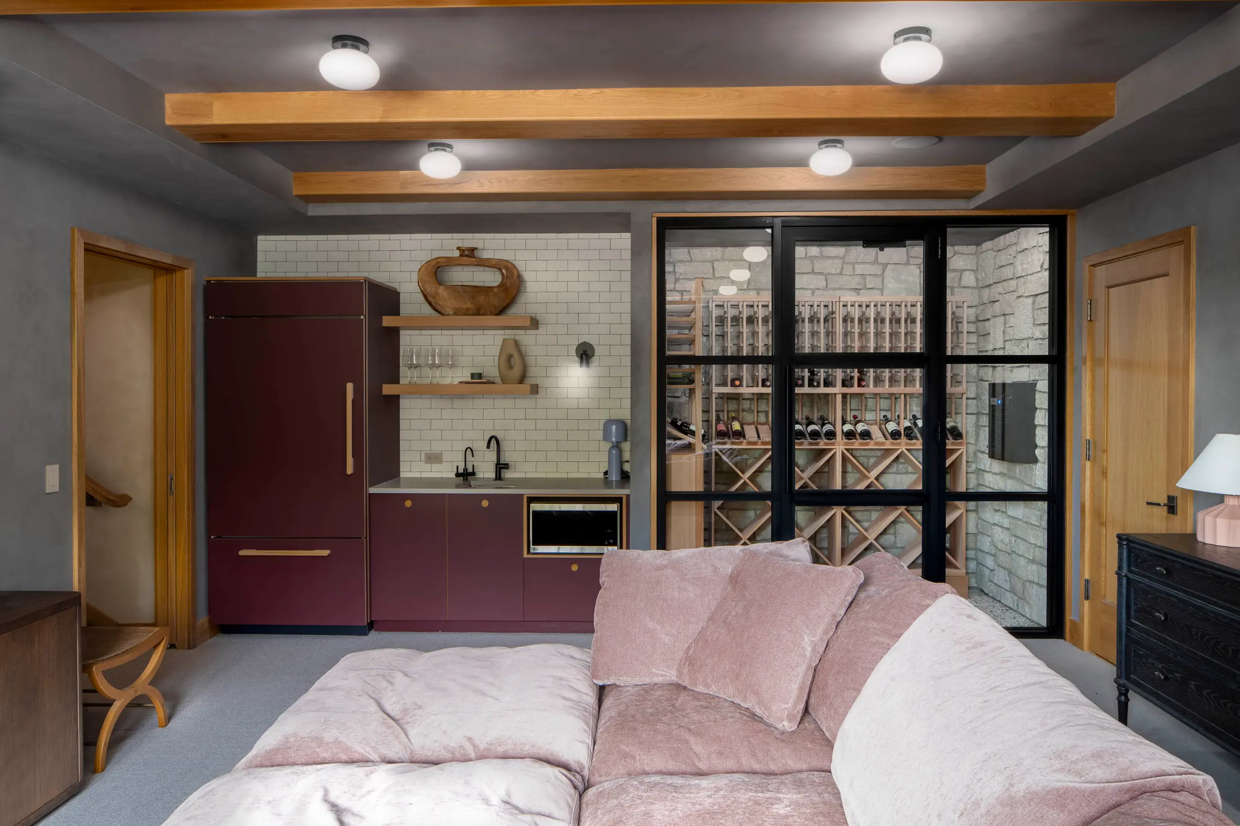 Modern living room with mauve sofa, kitchenette with burgundy cabinets, and glass wine cellar.