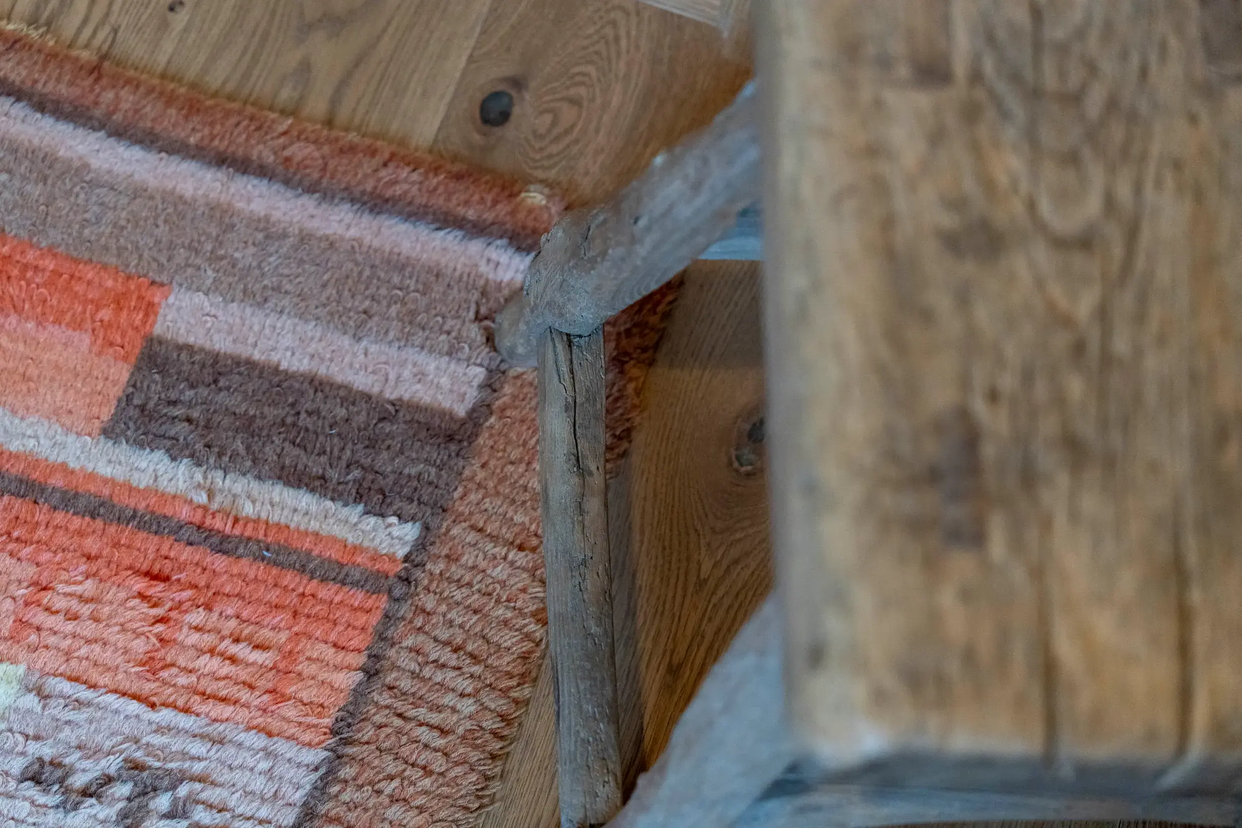 Close-up of wooden chair leg on a colorful woven rug and hardwood floor.