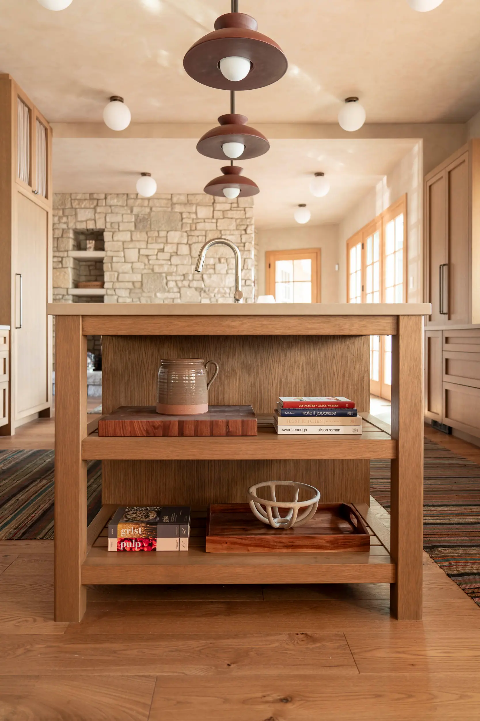 Wooden kitchen island with shelves holding pottery, books, and a tray in a rustic kitchen.