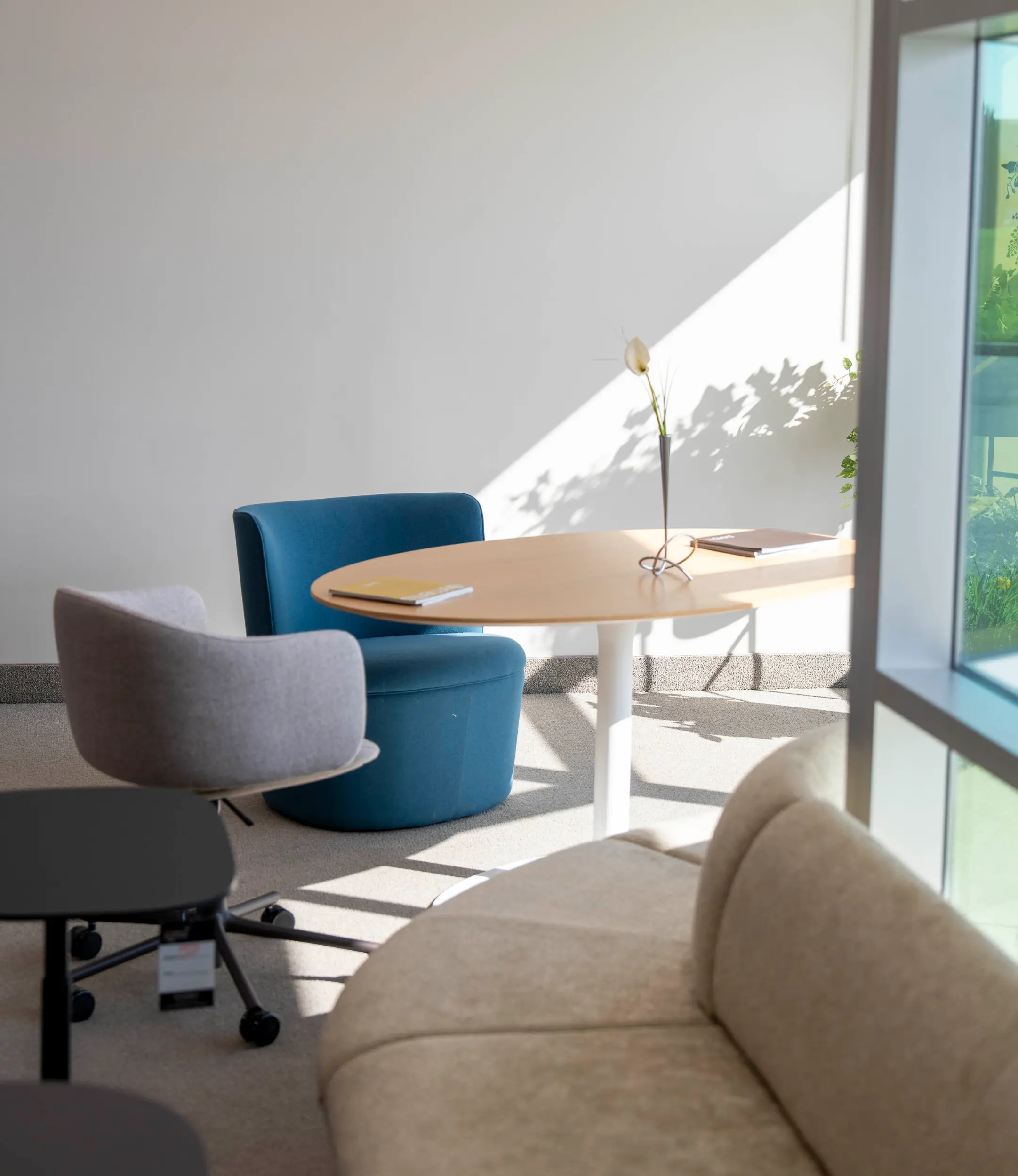 Modern office corner with a beige sofa, gray swivel chair, blue armchair, and round wooden table.