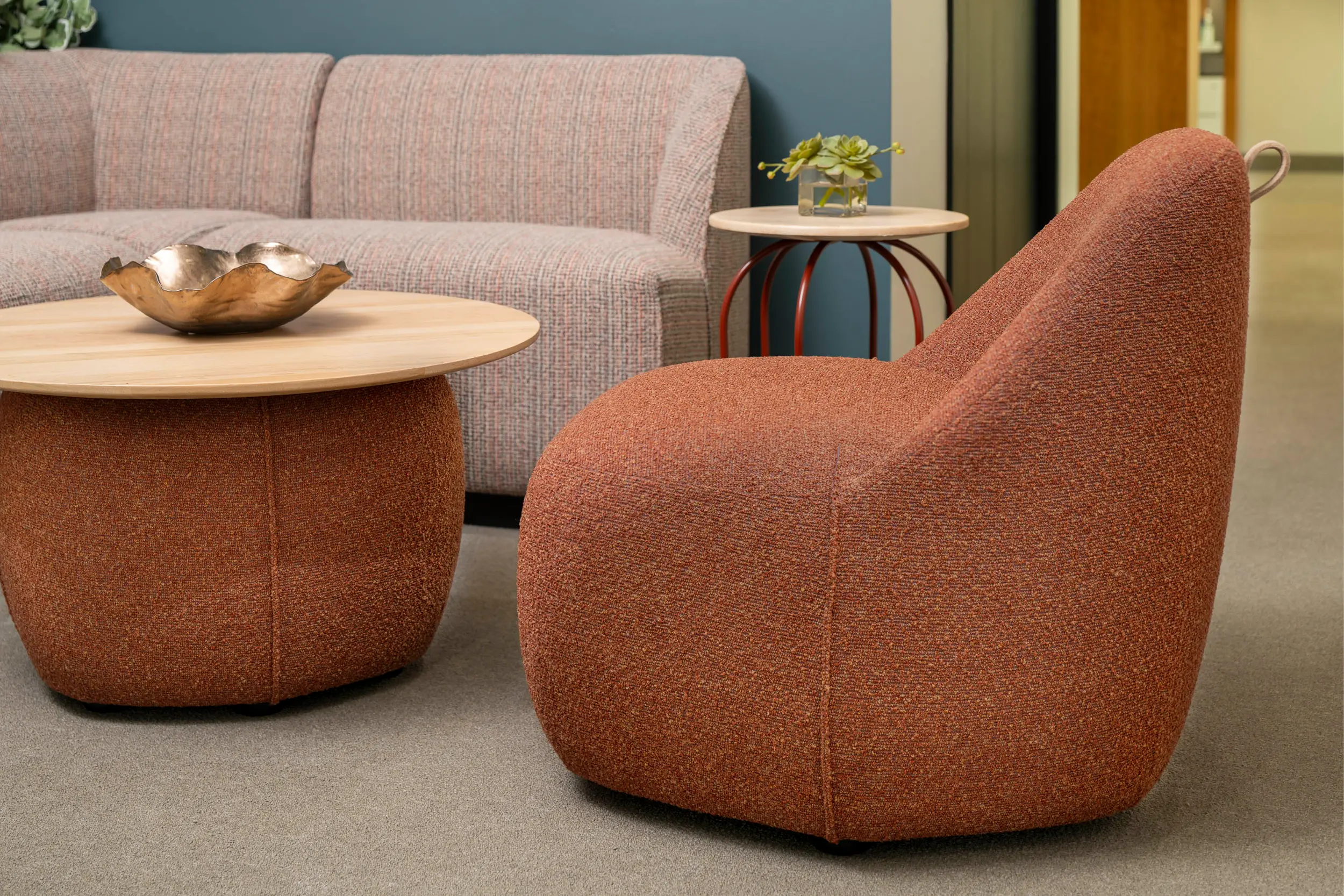 Cozy seating area with a textured rust-colored armchair, matching ottoman, sofa, and two round tables.