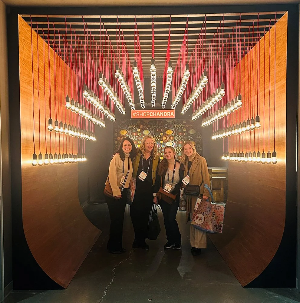 Four women standing in a tunnel of hanging light bulbs with a #SHOPCHANDRA sign above them.