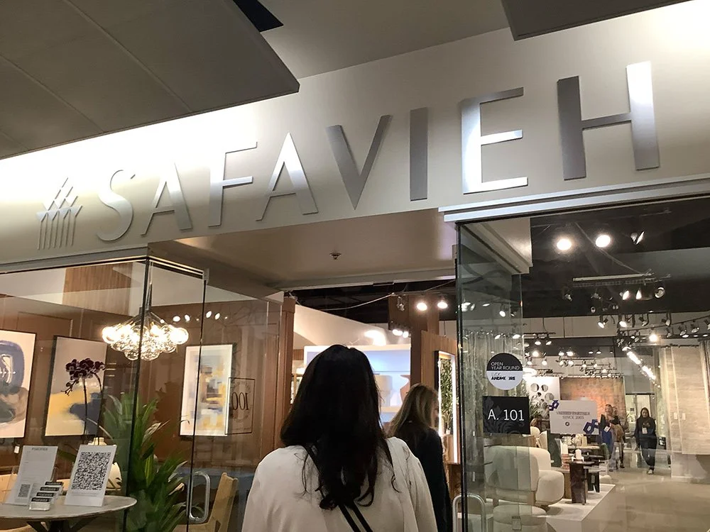 Woman entering a showroom with large 'SAFAVIEH' sign above the entrance and art inside.