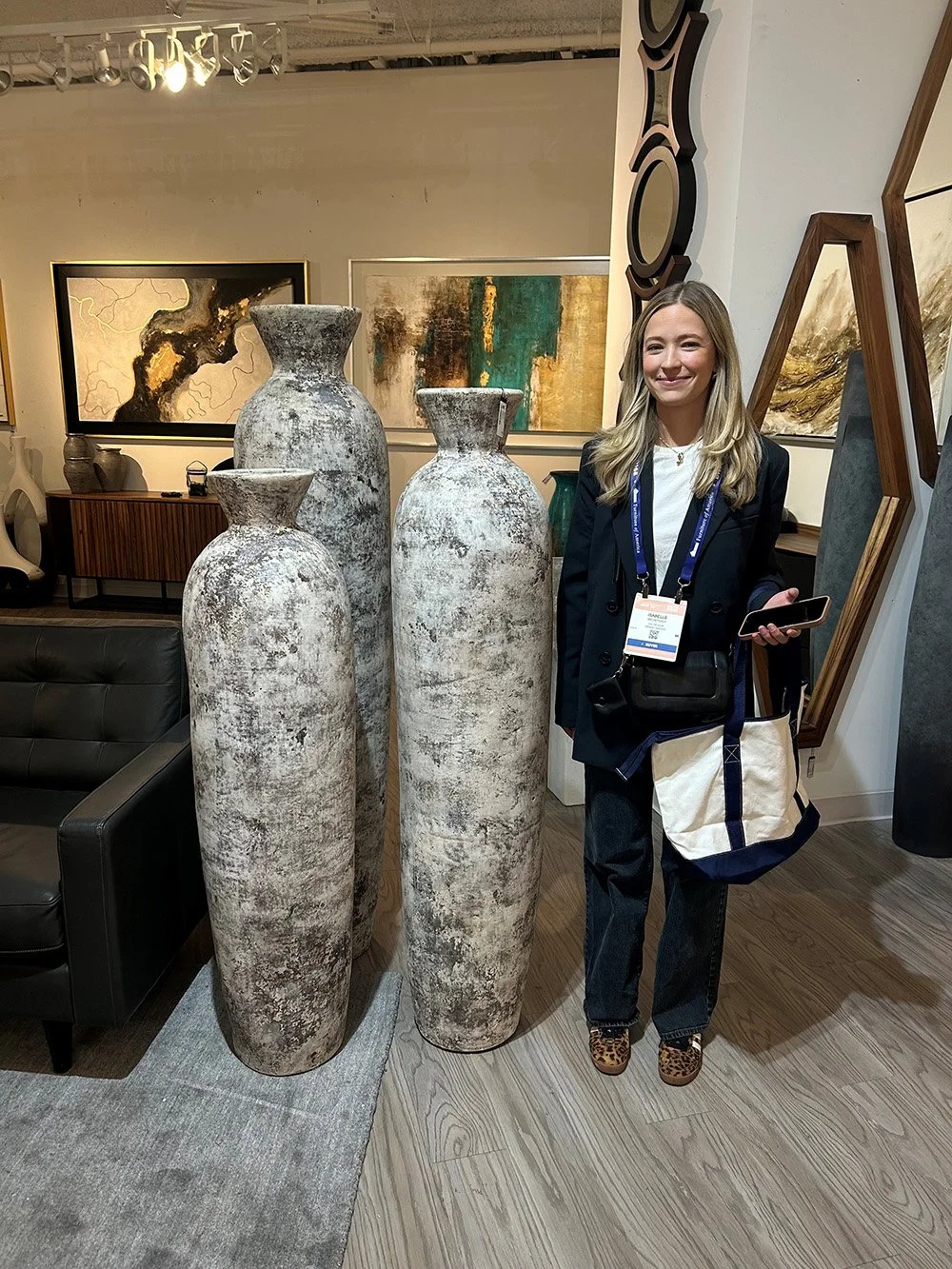 Woman standing next to three large ceramic vases in a gallery with abstract wall art.
