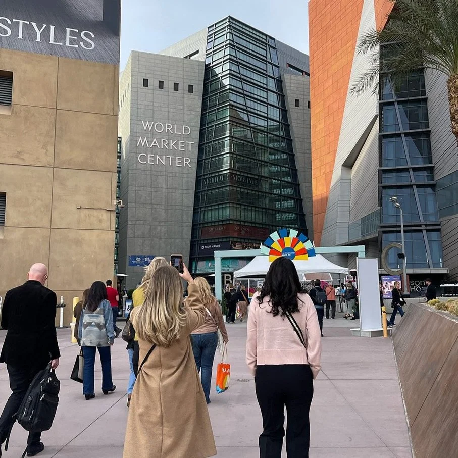 People walking toward World Market Center building with a colorful arch and tents outside.
