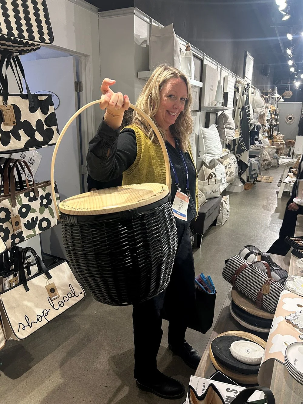 Woman in a store holding up a black woven basket with a wooden lid and handle.