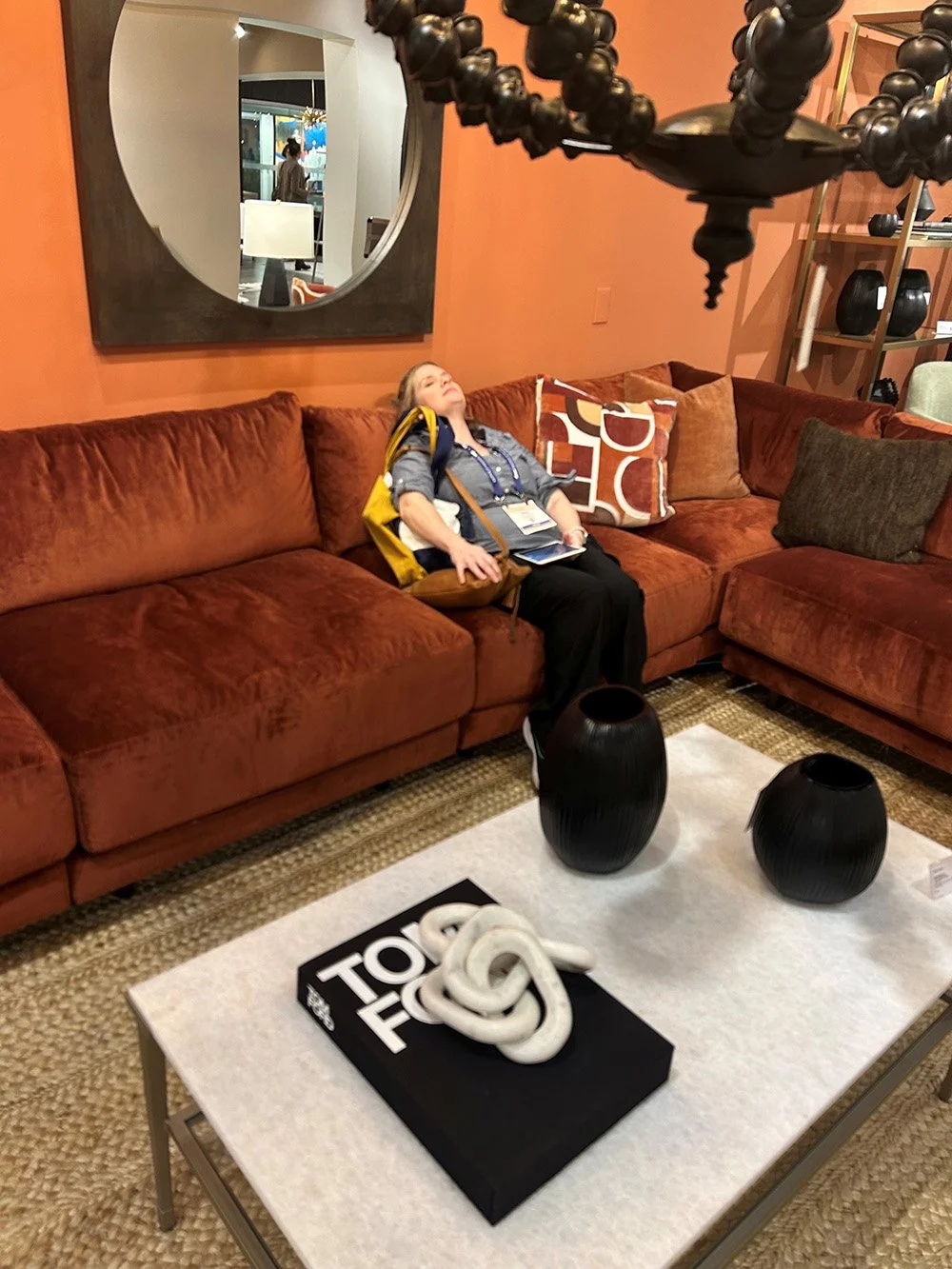 Person relaxing on a rust-colored sectional sofa with patterned pillows and a modern coffee table.