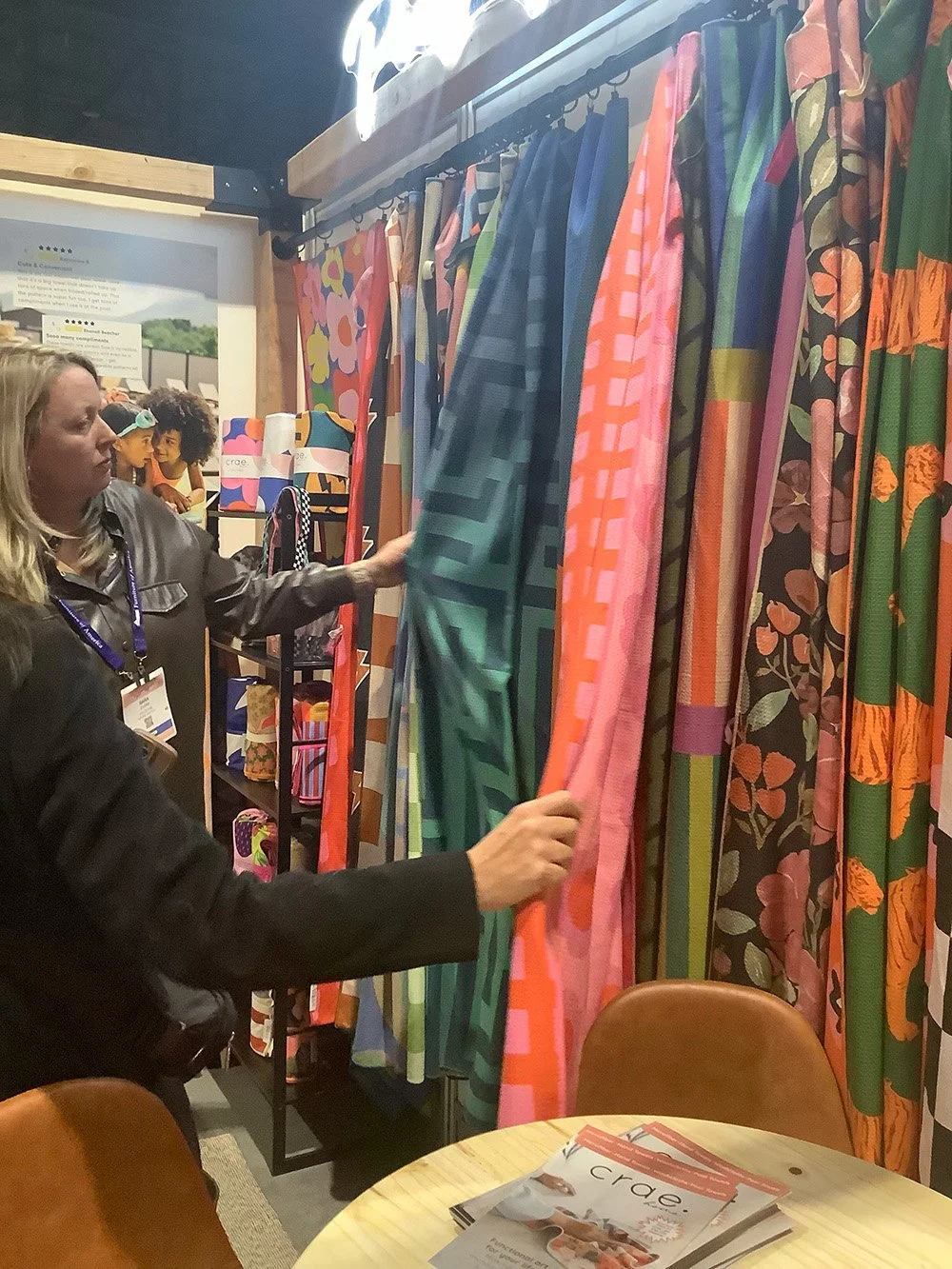 Two women examining colorful patterned fabrics hanging on display at a booth or store.
