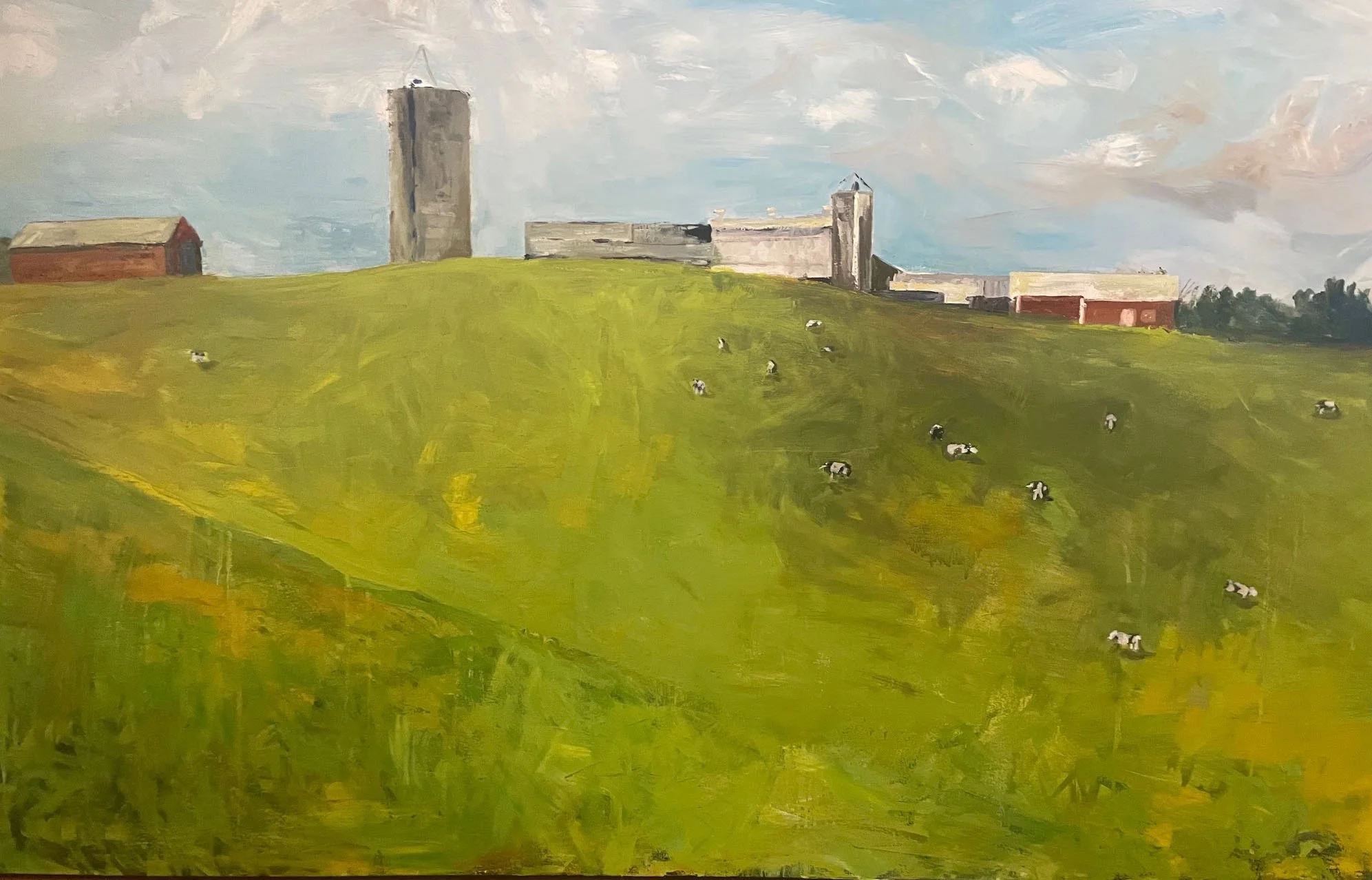 Green hill with grazing cows and farm buildings under a cloudy sky.