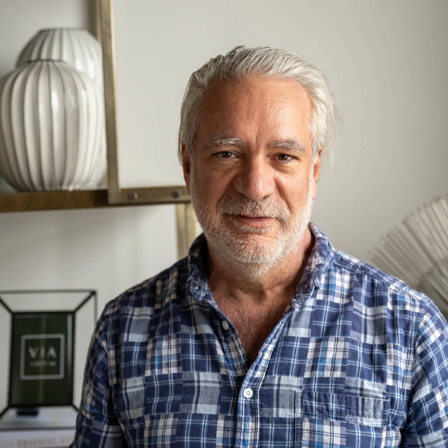 Smiling middle-aged man with gray hair and beard wearing a blue plaid shirt indoors.