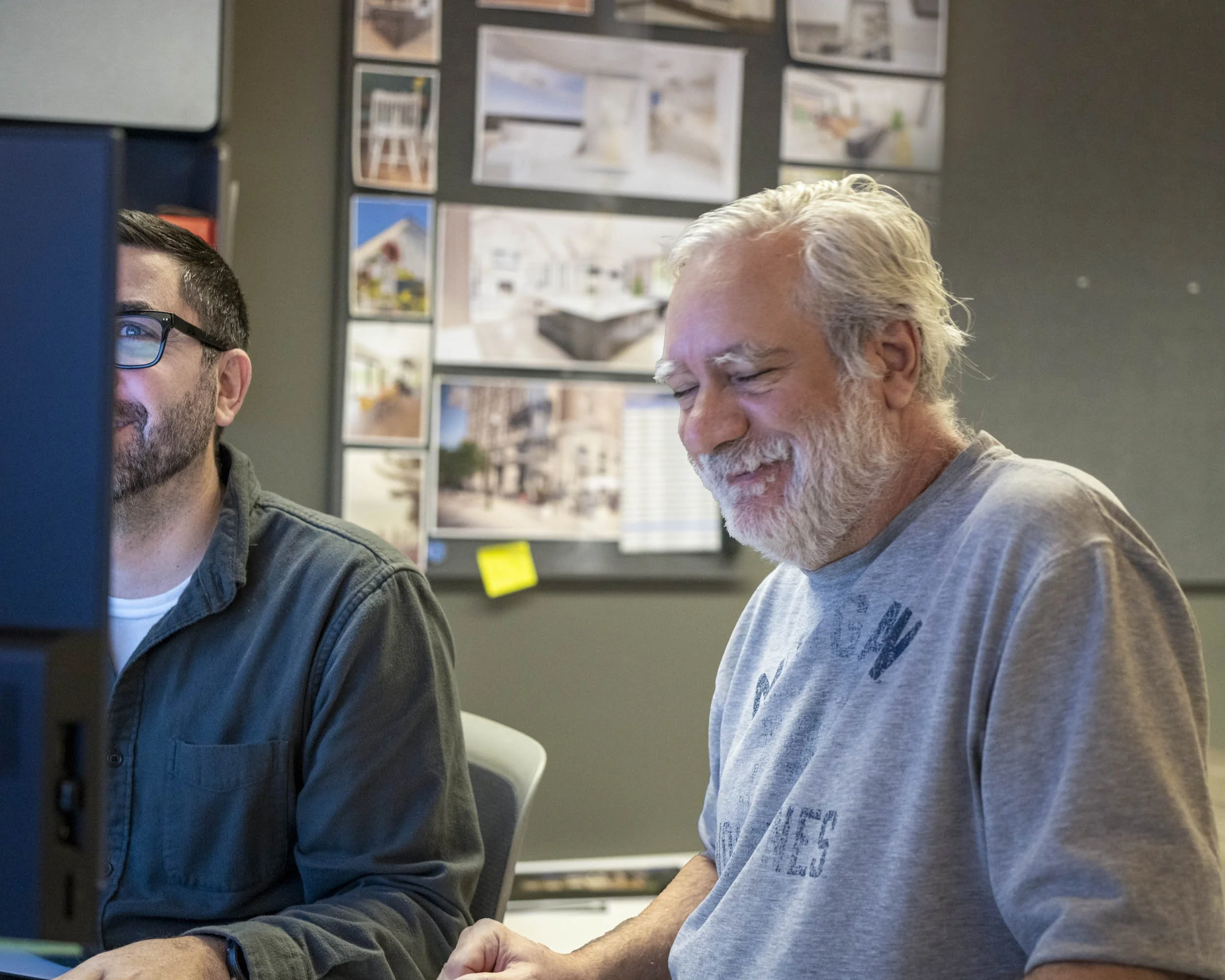 Two men in an office looking at a computer screen, one smiling and one concentrating.