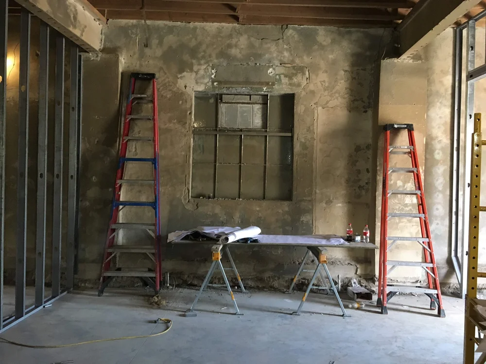 Two ladders and a workbench with rolled blueprints against a rough unfinished wall in a construction site.