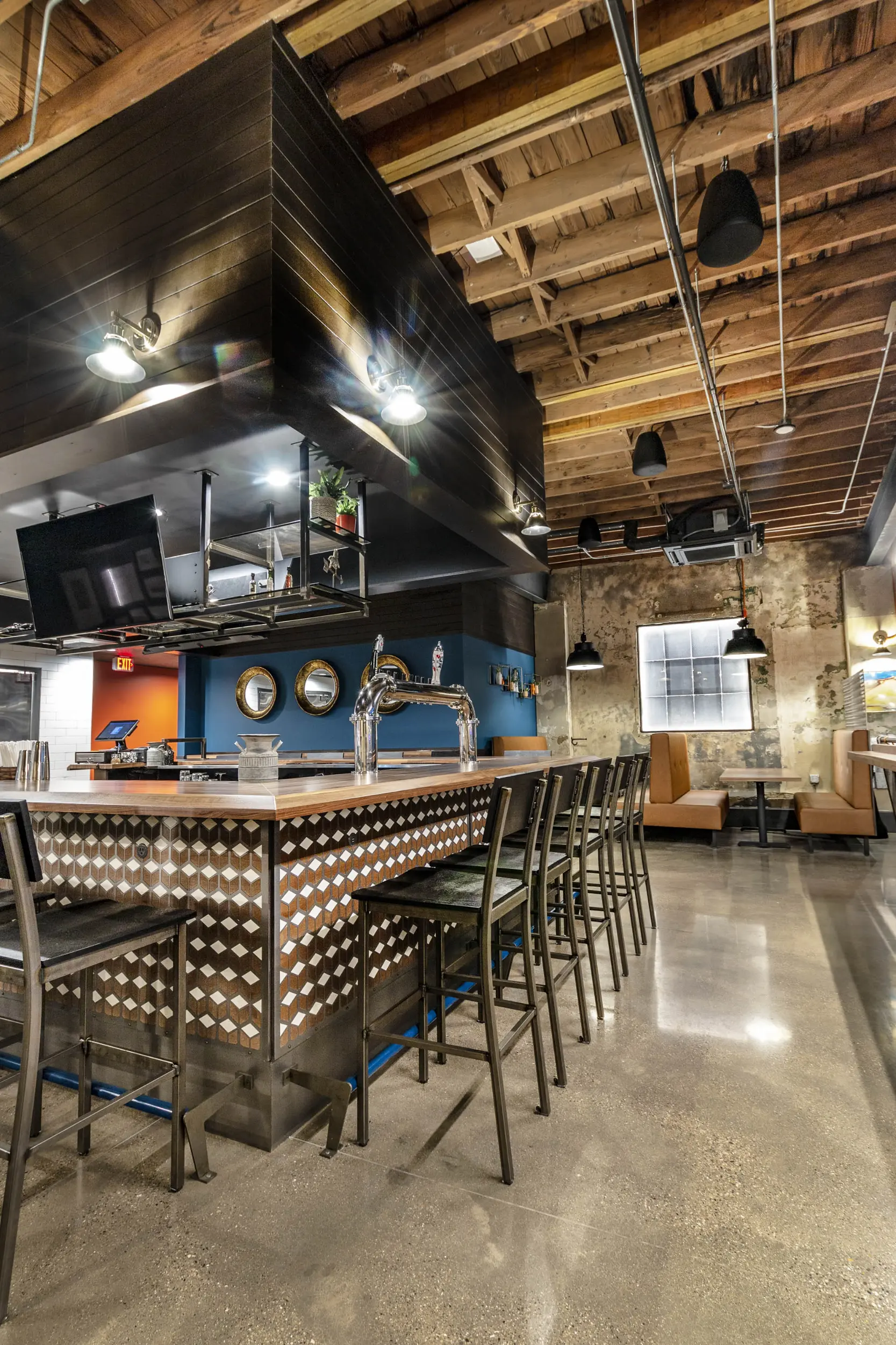 Modern bar with high chairs, patterned wood countertop, pendant lights, and exposed wooden ceiling beams.