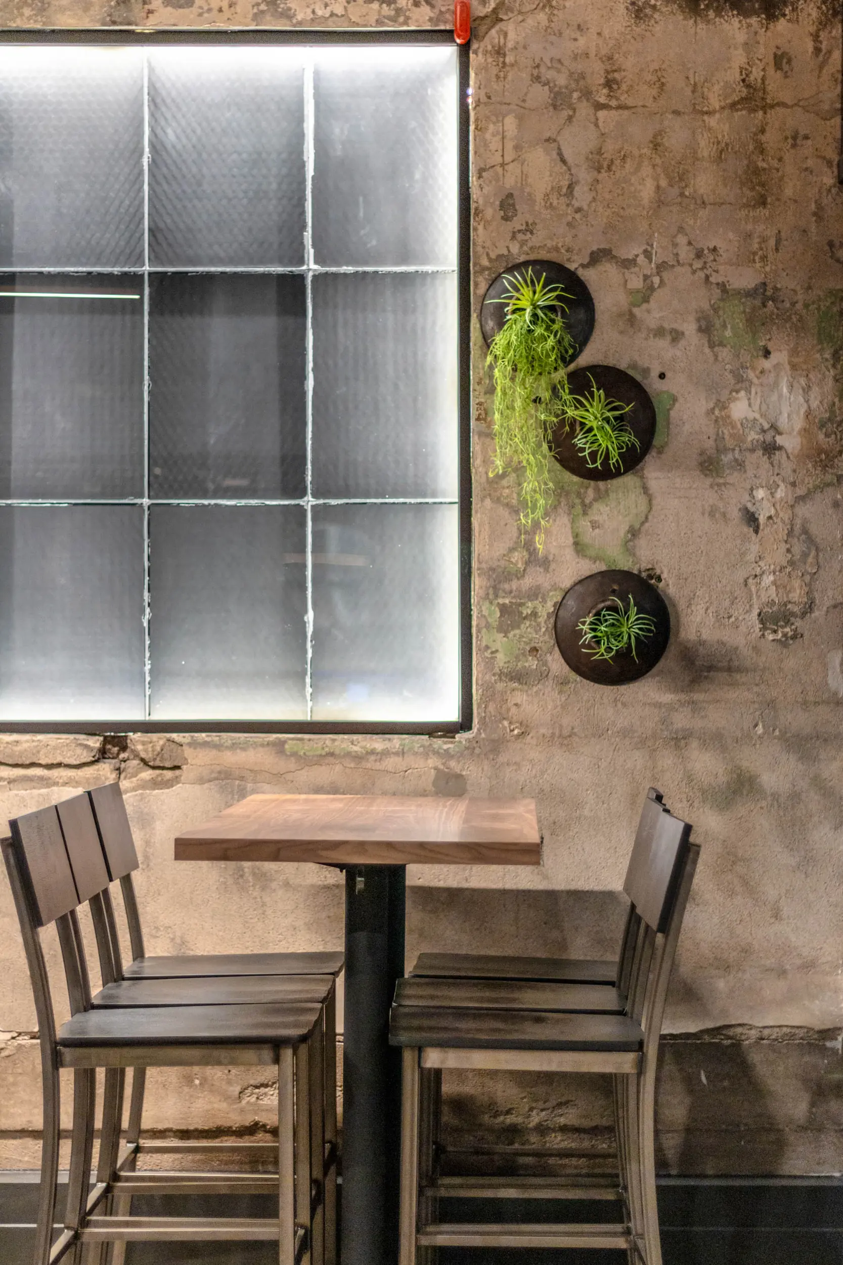 Wooden table with four metal chairs in front of a textured wall with three small hanging plants.