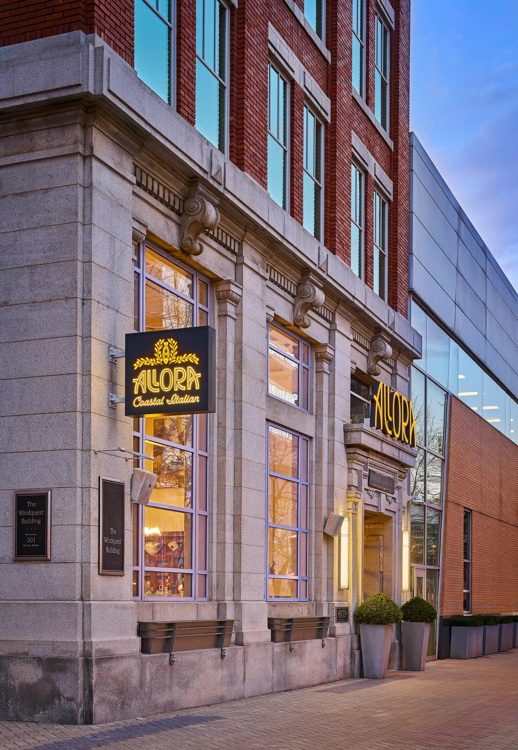 Entrance of Allora Coastal Italian restaurant in a brick and stone building at dusk.