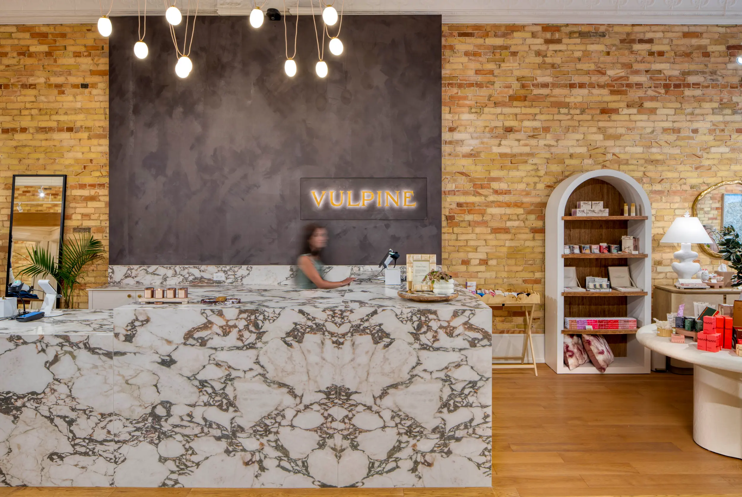 Store interior with marble counter, brick walls, hanging lights, and shelves with merchandise.