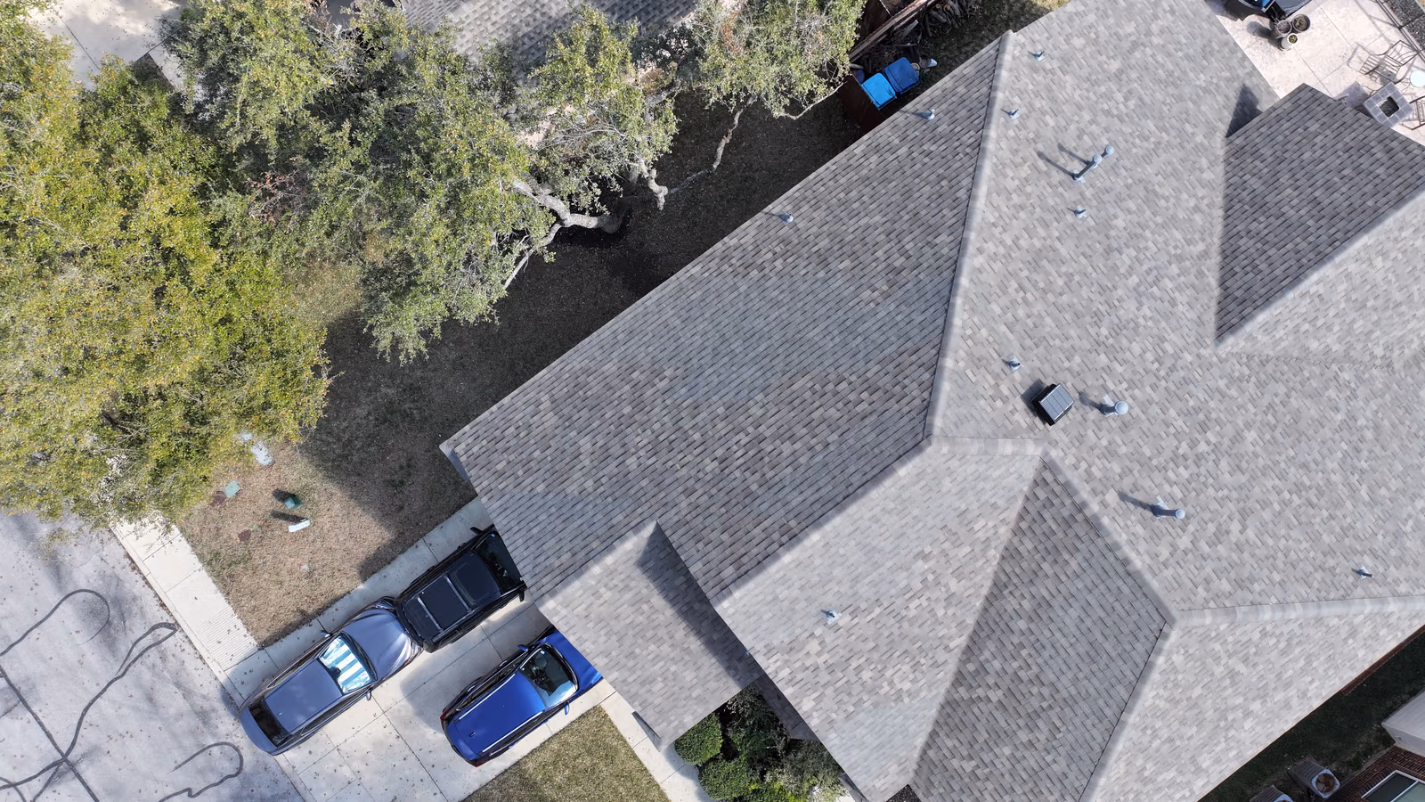 Aerial view of a gray shingle roof with a complex roofline on a suburban home.