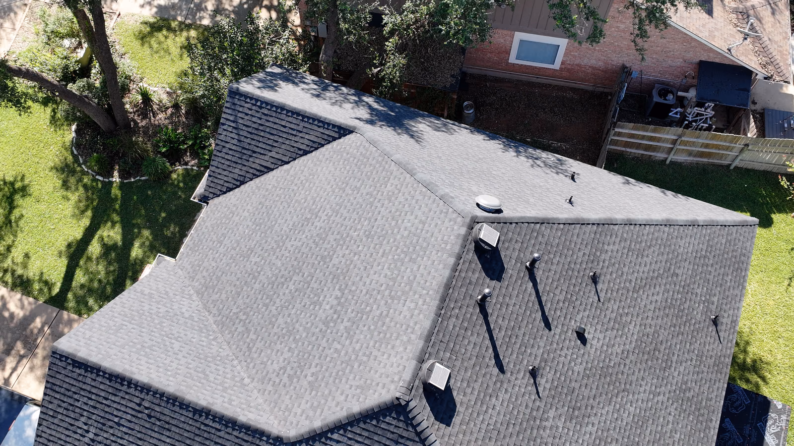 Aerial view of a finished gray shingle hip roof surrounded by trees.