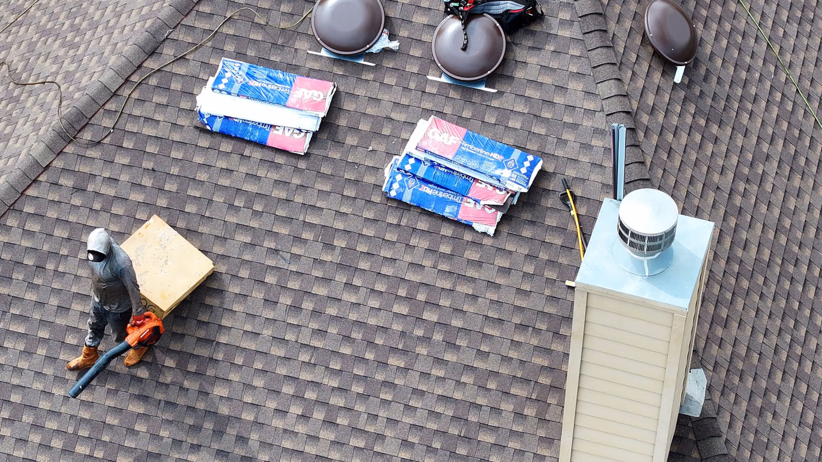 Roofer performing maintenance work with materials staged on a shingle roof.