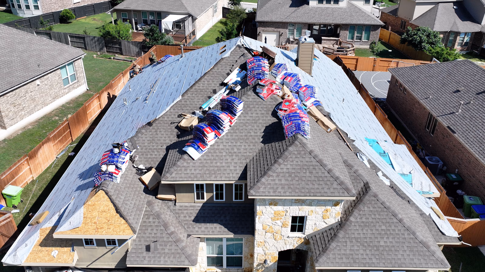 Roofing materials and a staging canopy set up at an organized job site.