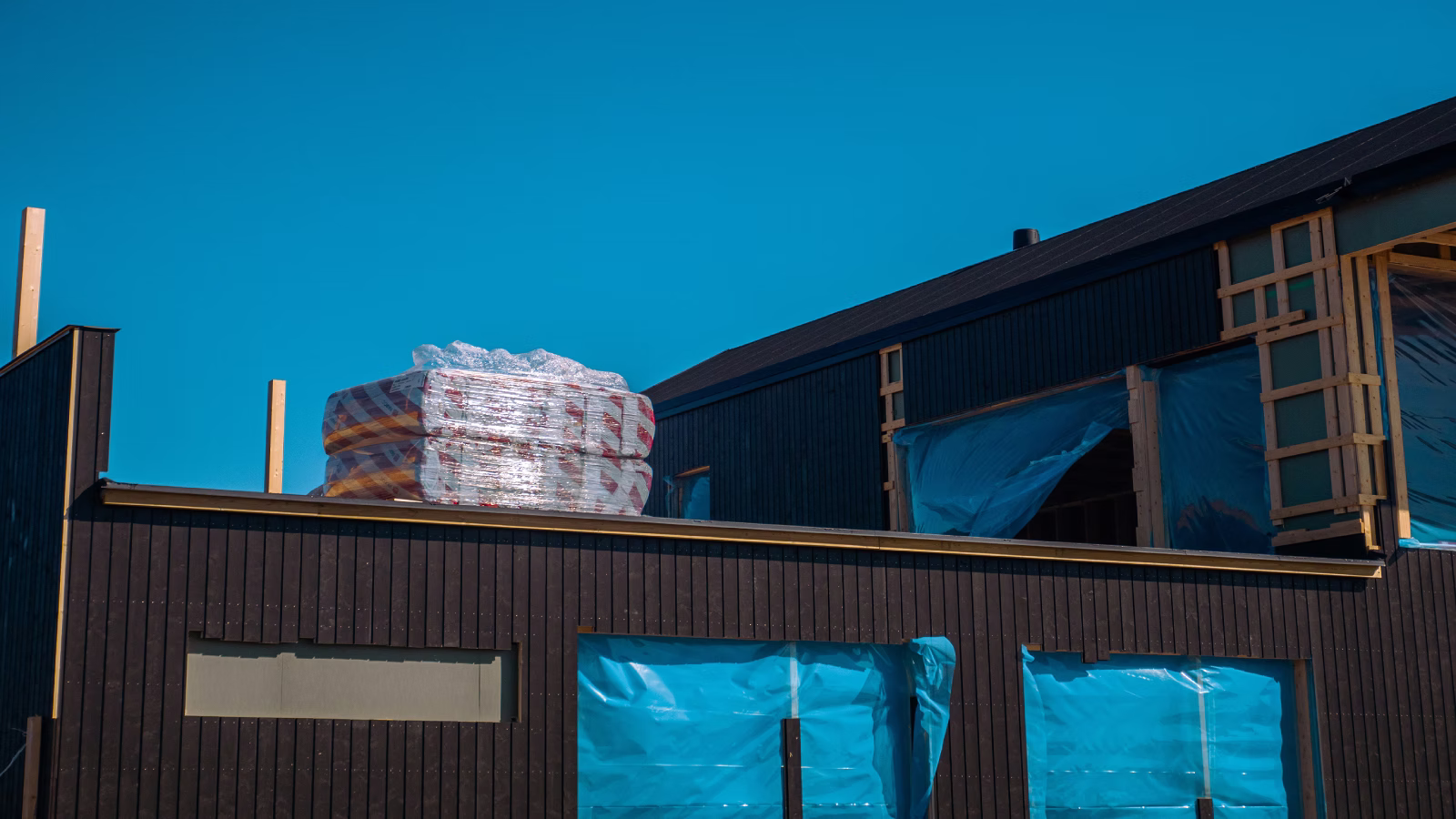 Building under construction with window openings covered in blue plastic sheeting.