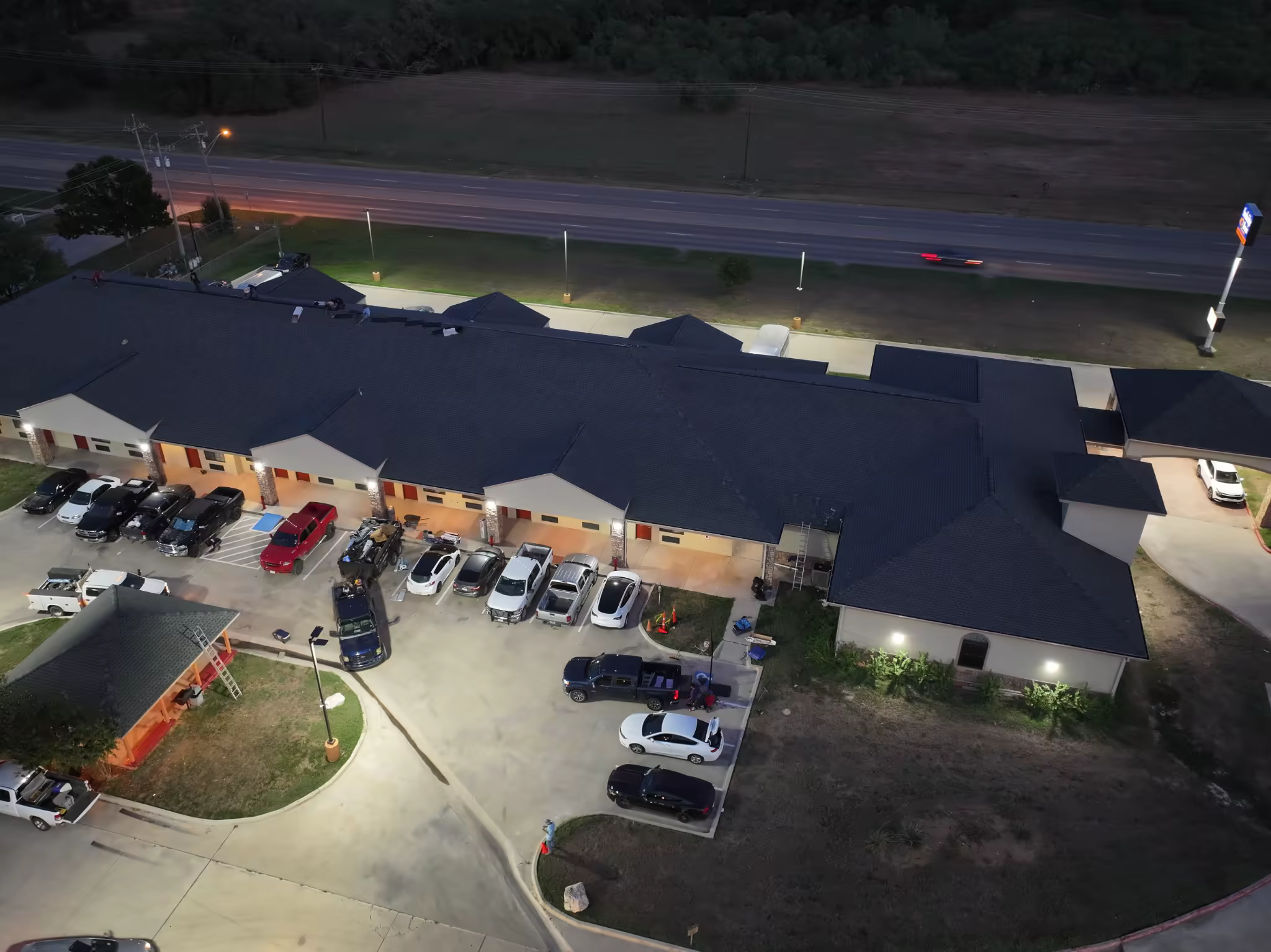 Aerial view of roofing work underway at Sunbridge Inn & Suites after sunset