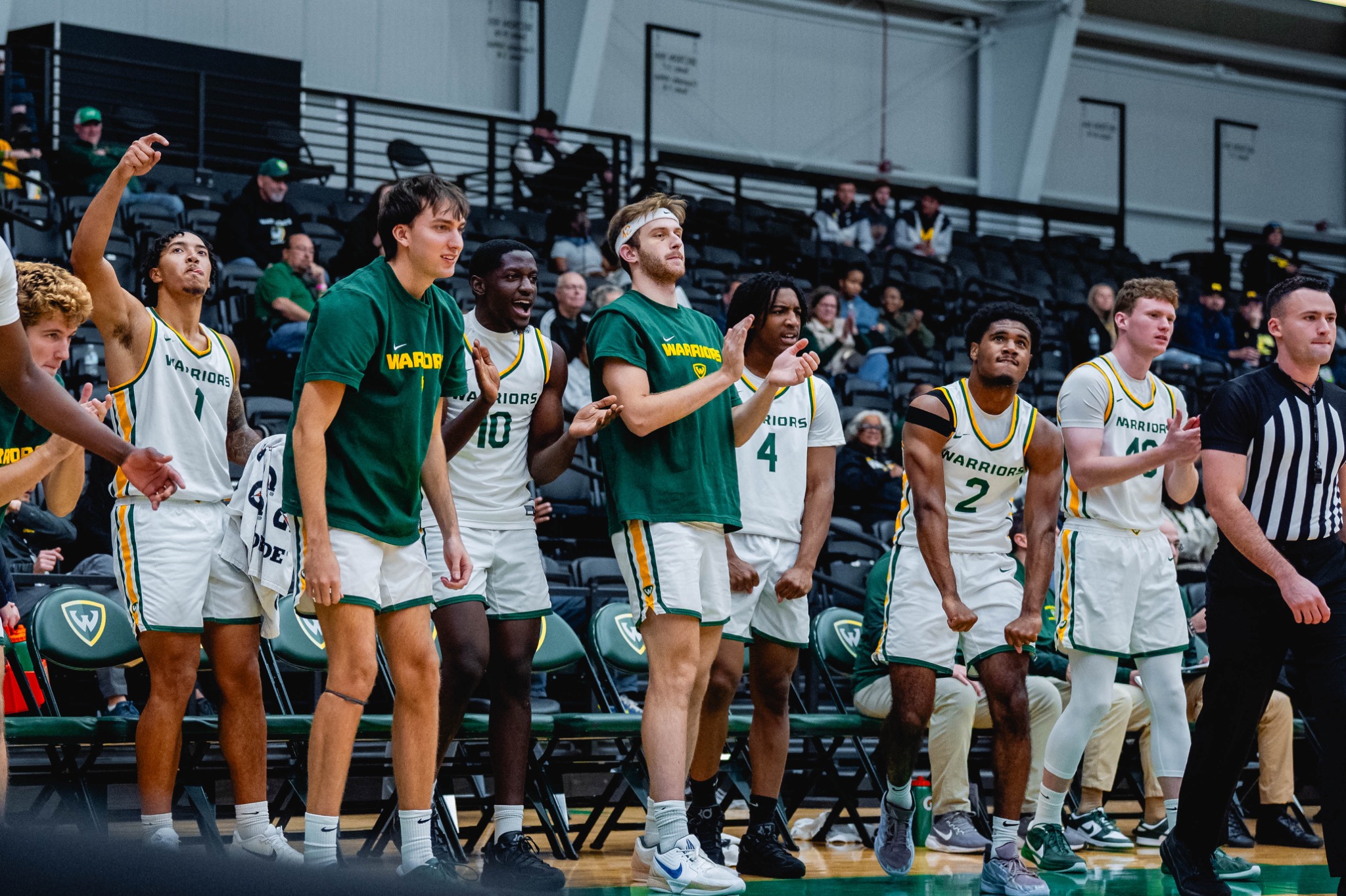 Wayne State men’s basketball players cheer from the sideline.