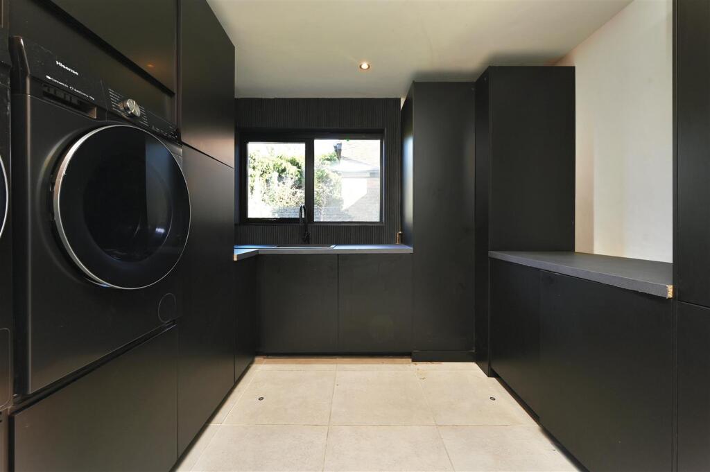 Modern laundry room with black cabinets, stacked washer and dryer, and window above a sink.