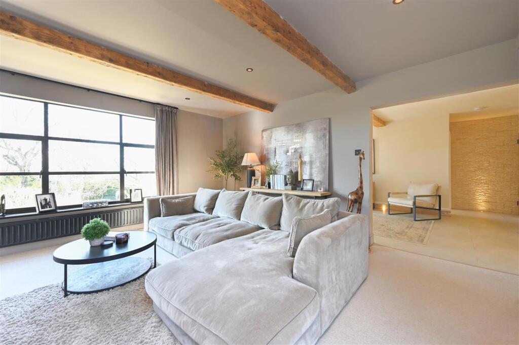 Bright living room with a large gray sectional sofa, round coffee table, and wooden ceiling beams.