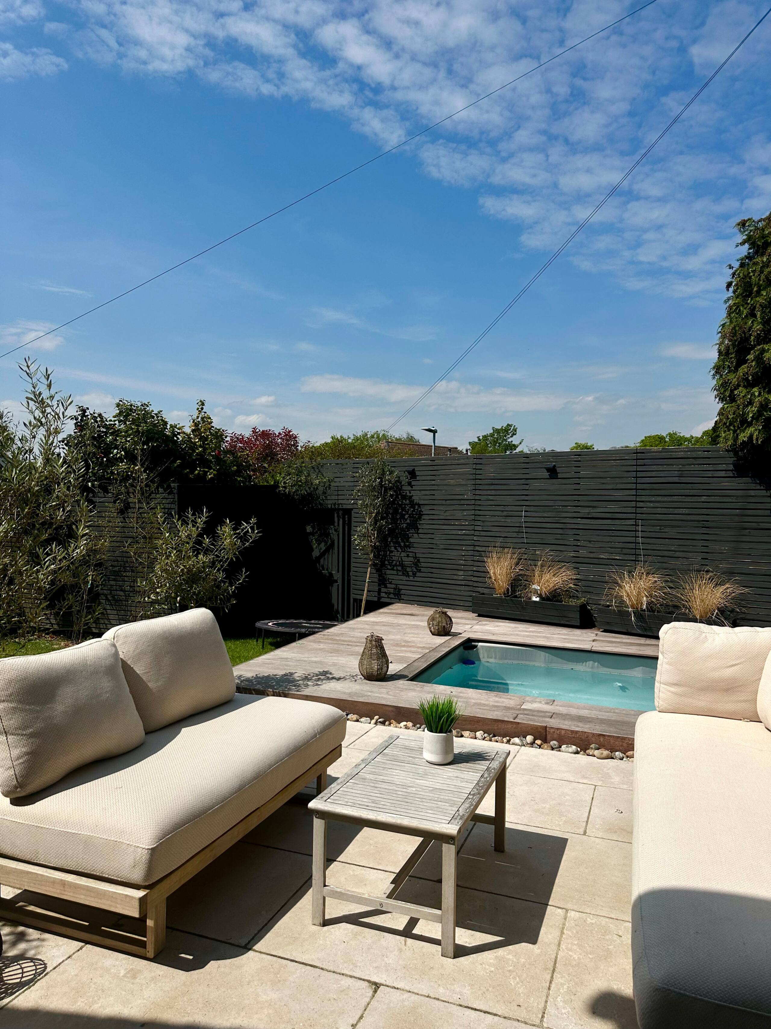 Outdoor patio with beige cushioned sofas, a small wooden table, and a small pool surrounded by wood decking.
