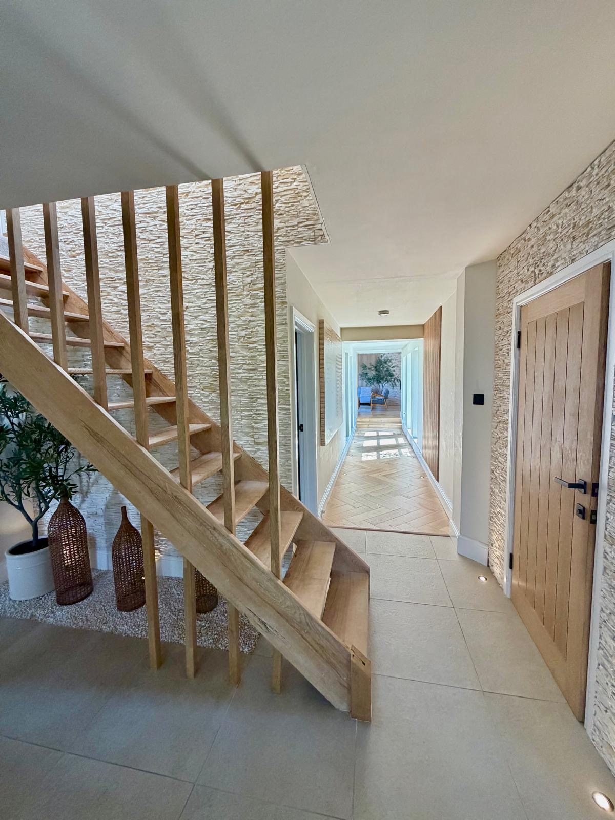 Interior hallway with wooden staircase, textured stone walls, tiled floor, and a potted plant.