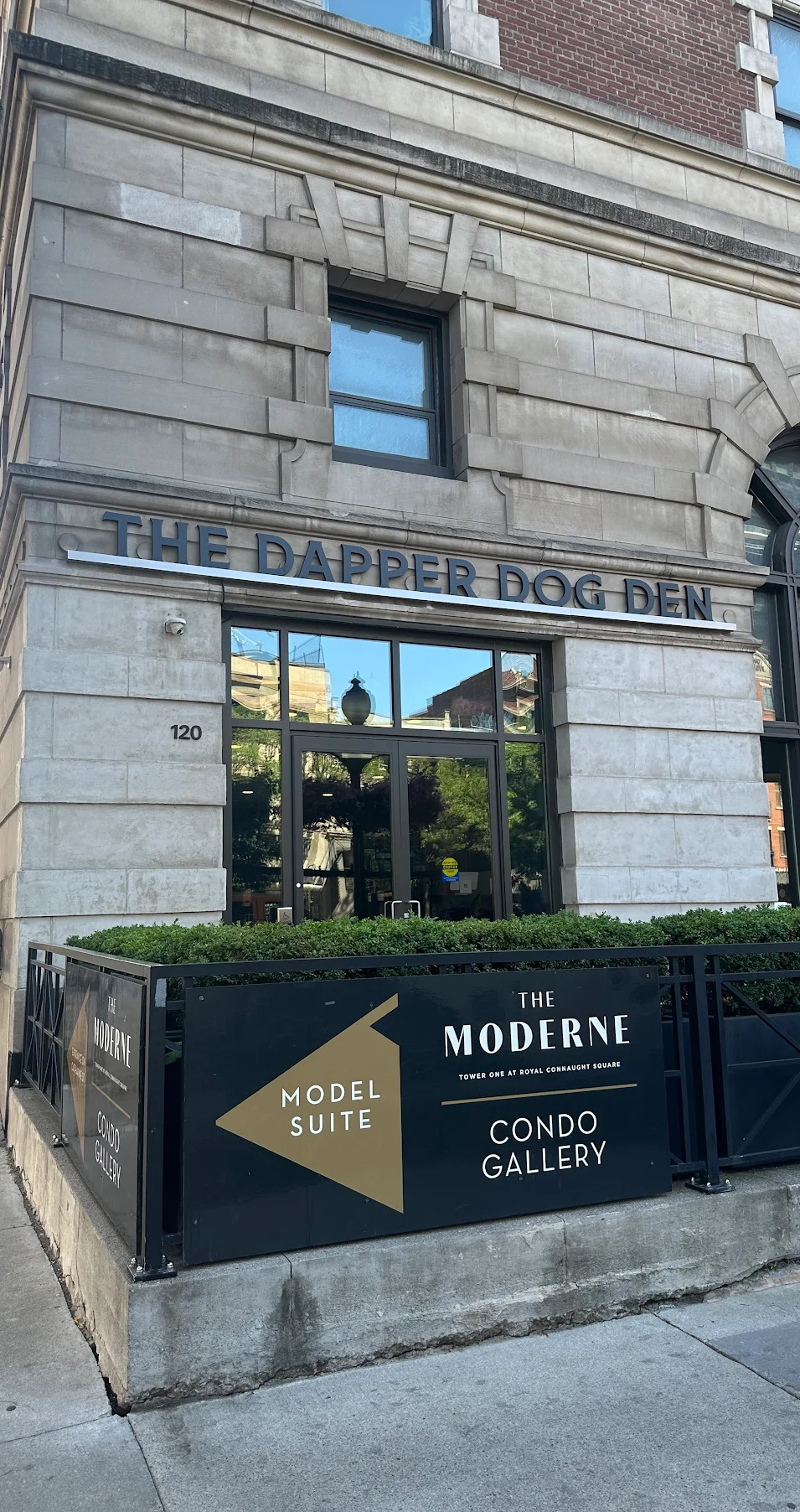 Entrance of The Dapper Dog Den at 120 with a sign for The Moderne condo gallery and model suite.