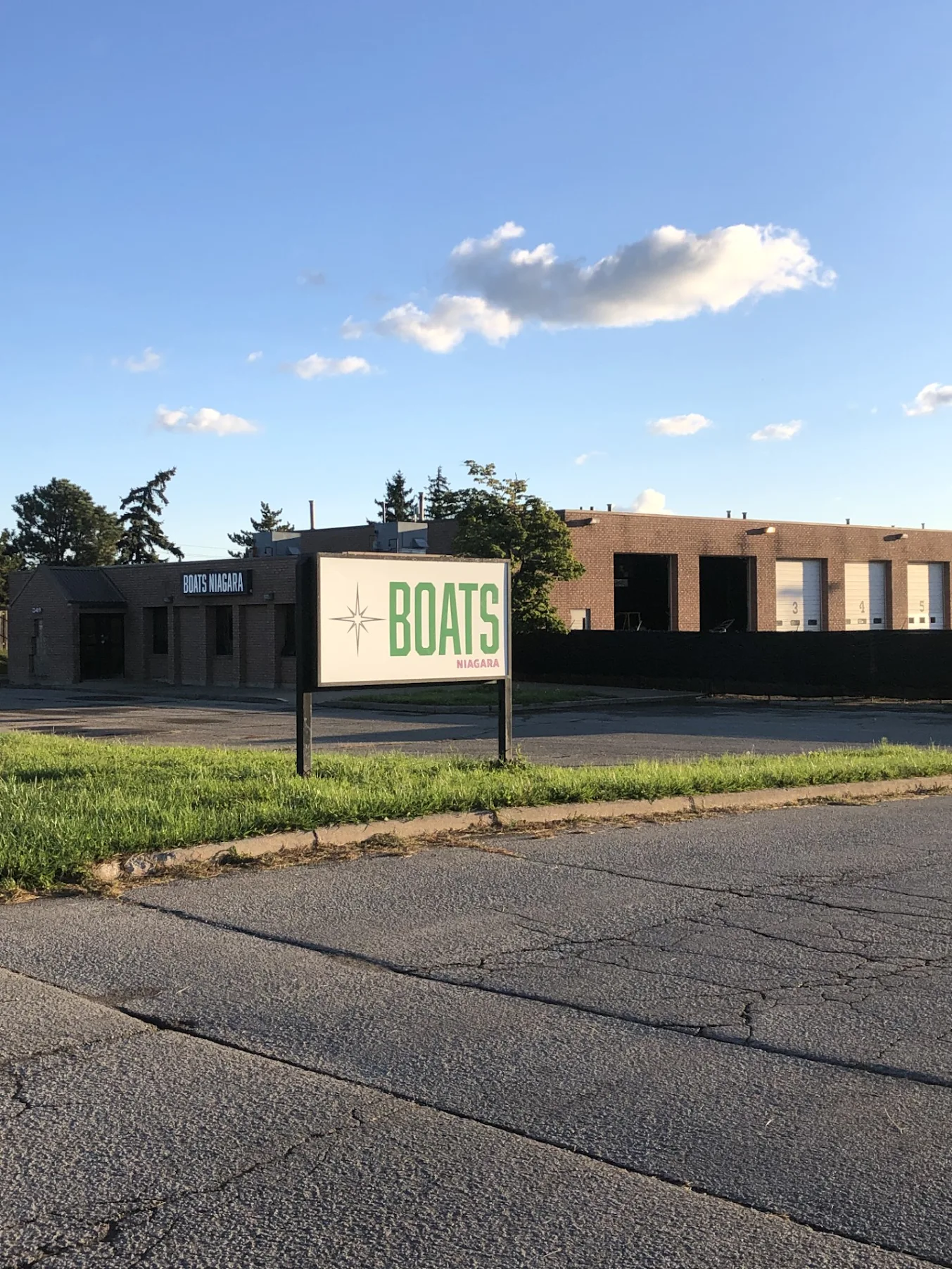 Commercial building with a sign reading Boats Niagara on a cracked pavement street under a blue sky.