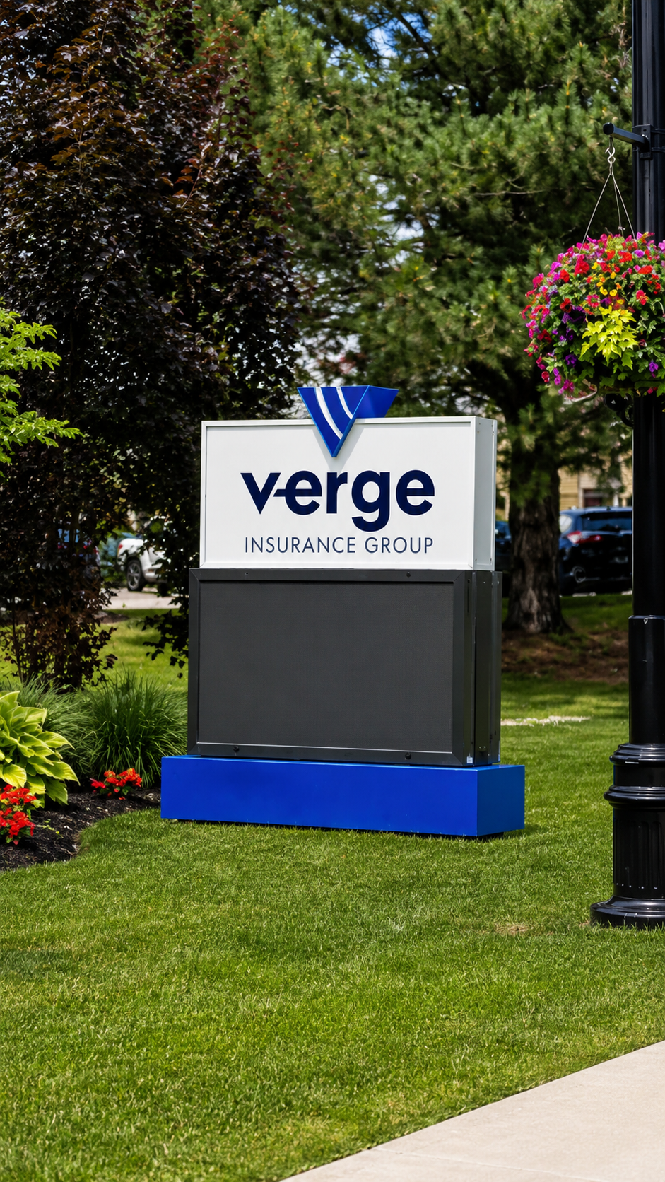 Sign for Verge Insurance Group on grass with trees and flowers around it.