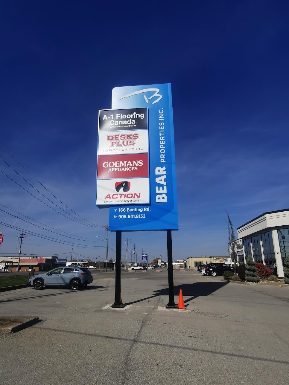 Tall blue signboard listing businesses near parking lot under clear blue sky.