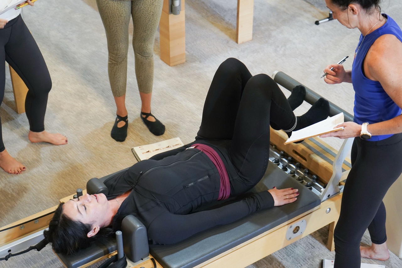 image of a Pilates student practicing on the Pilates Reformer while students observe and take notes