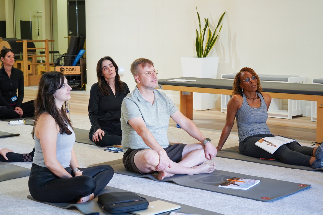 image of a group of students sitting on Pilates mats and paying close attention.