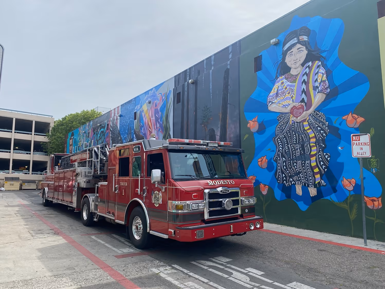 Red Modesto fire truck parked beside a building with colorful mural of a girl holding a heart.