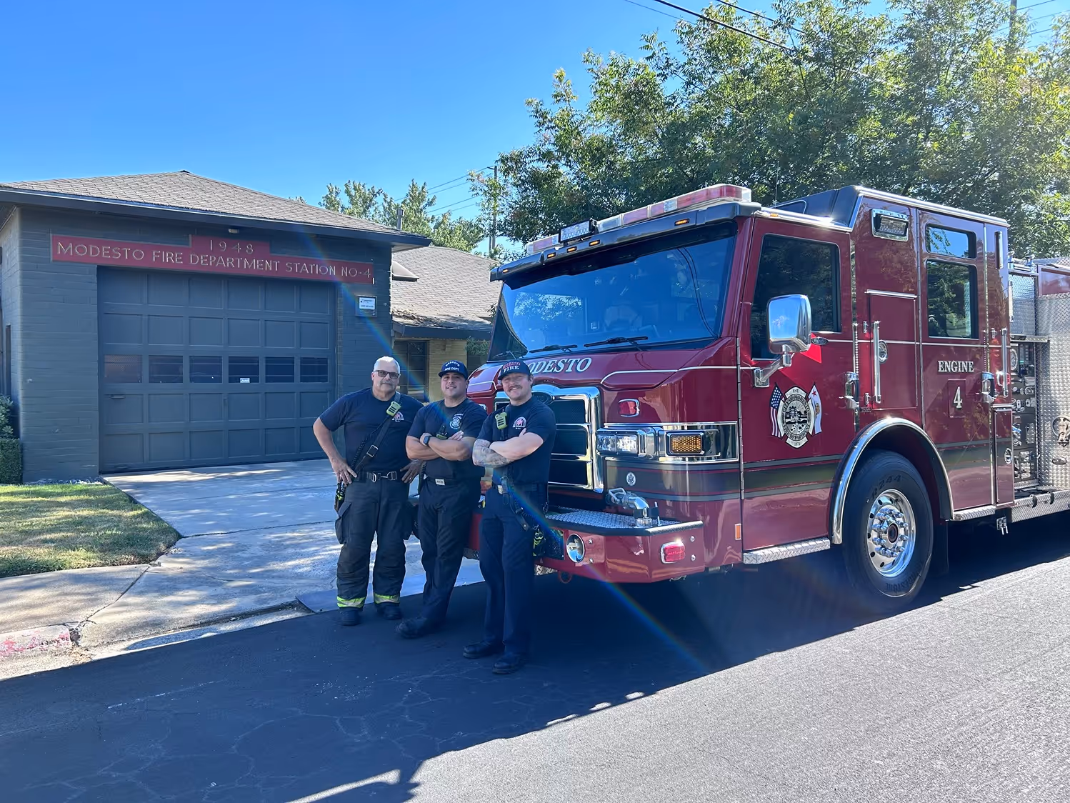 Three firefighters standing beside a red fire truck outside Modesto Fire Department Station No. 4.