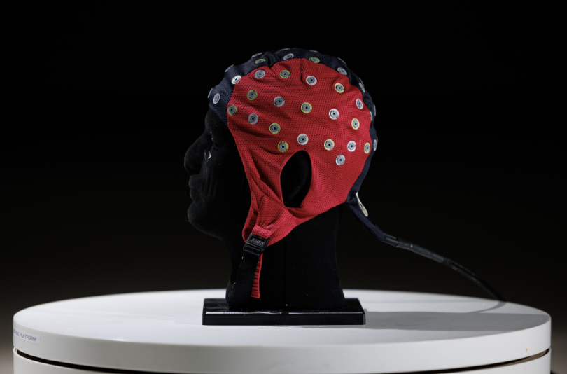 A mannequin head wearing a mobile Scalp EEG System. A soft helmet-like headpiece with many small round EEG leads all over.