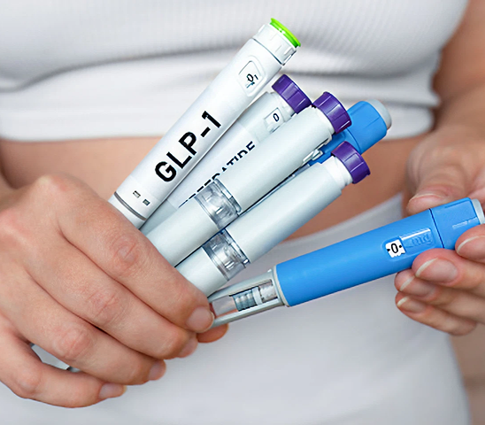 Person holding multiple injectable GLP-1 medication pens with various colored caps.