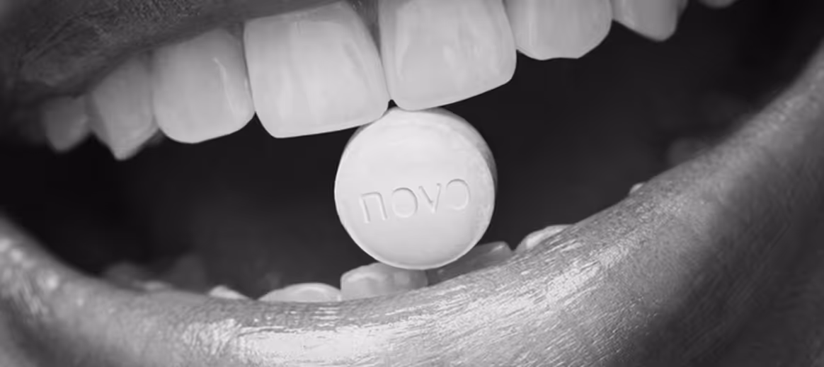 Close-up of open mouth holding a round pill with the text 'NOVA' embossed.